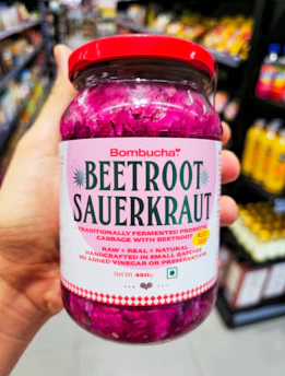 Hand holds jar of beetroot sauerkraut in store.