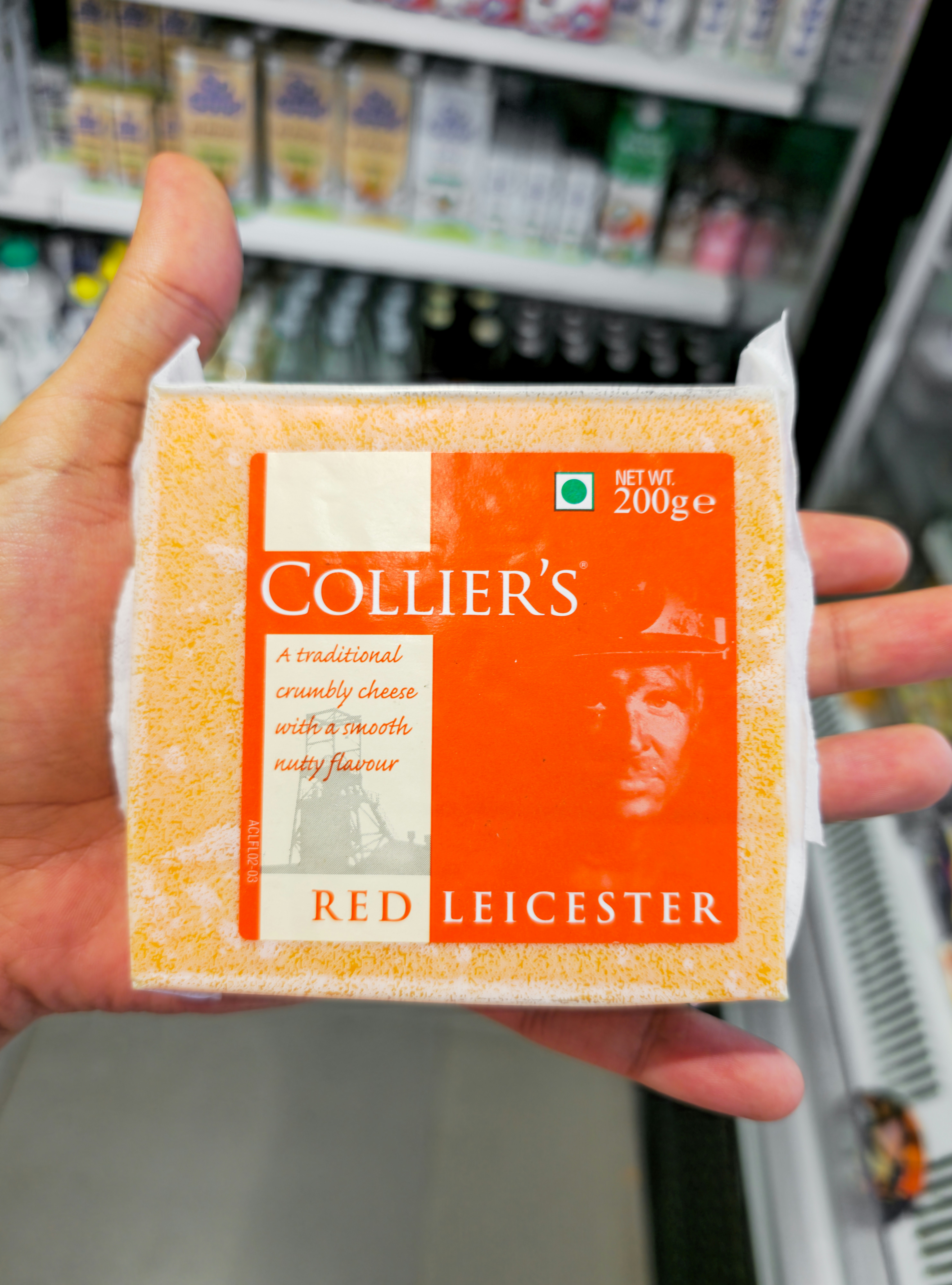 Hand holding collier's red leicester cheese block.