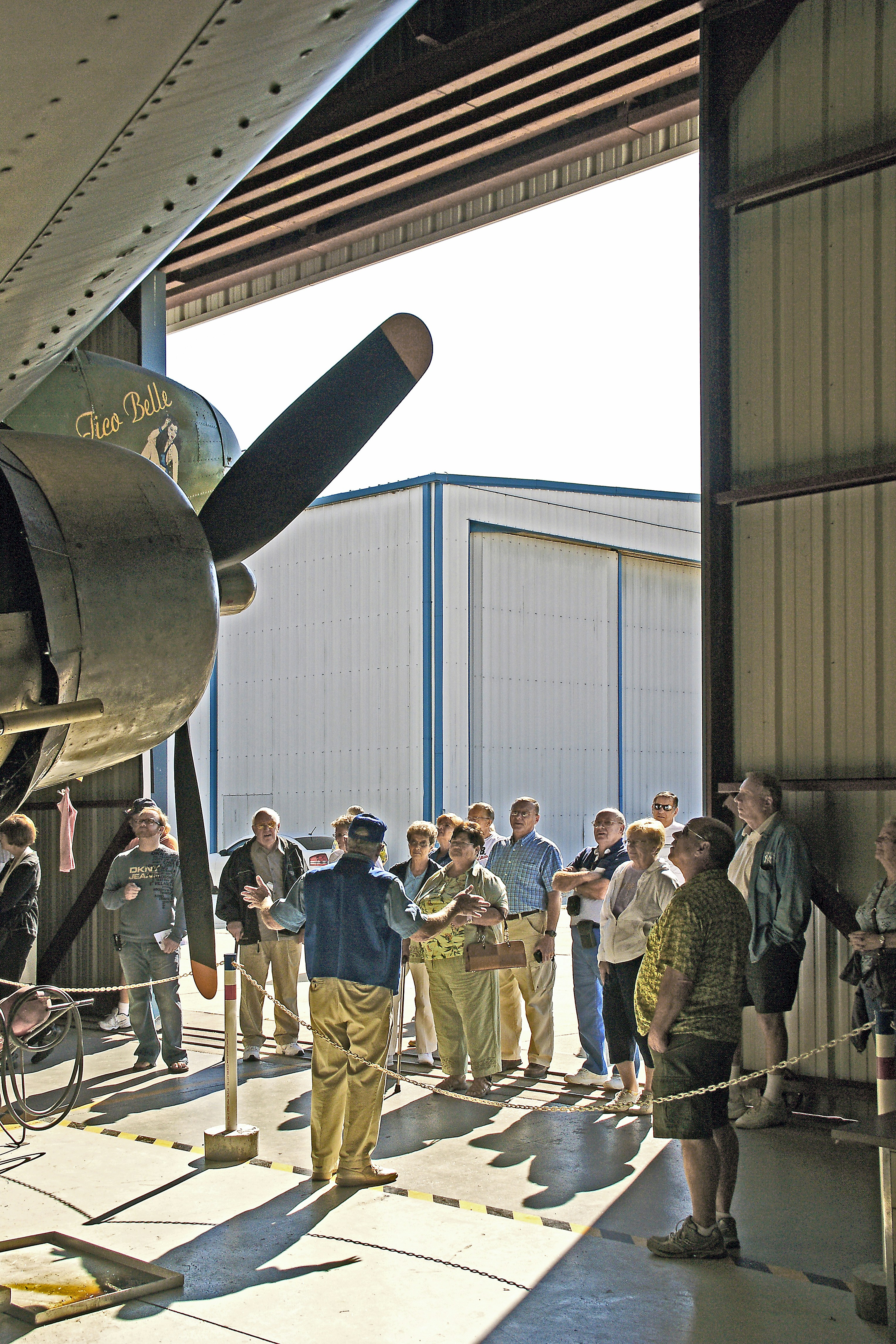 Tour group listens to guide by vintage airplane.