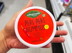Hand holding container of wingreens peri peri hummus