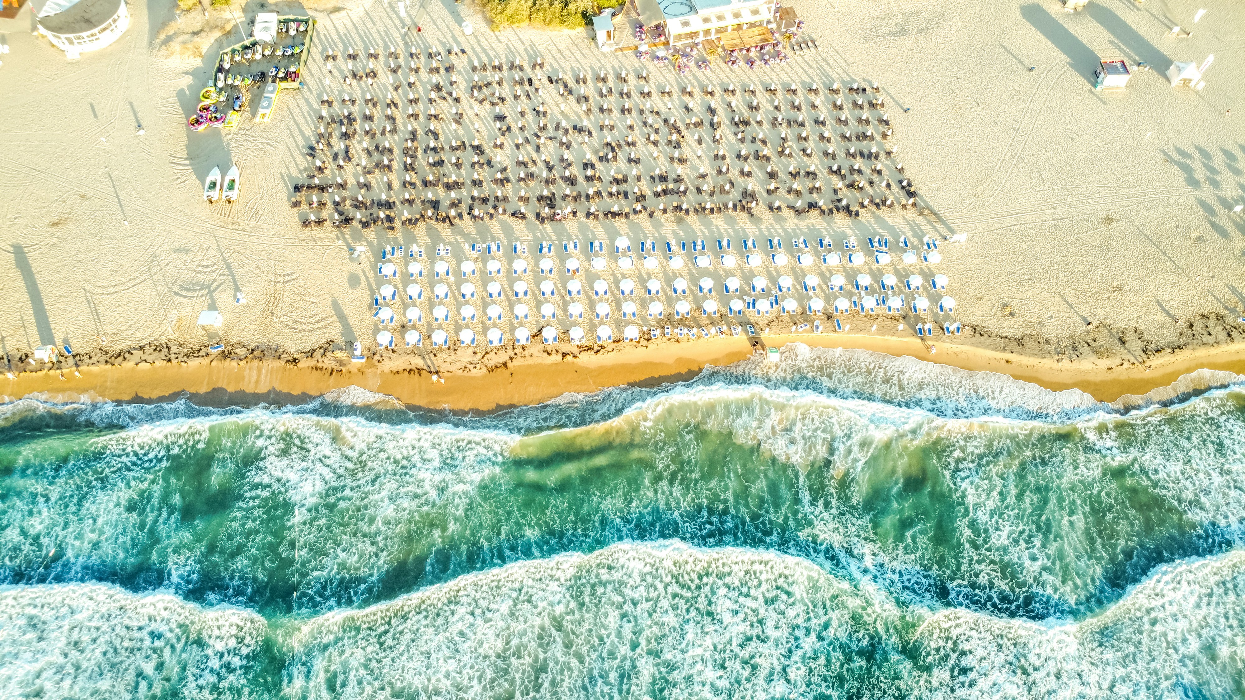 Rows of beach umbrellas on a sandy shore with waves.
