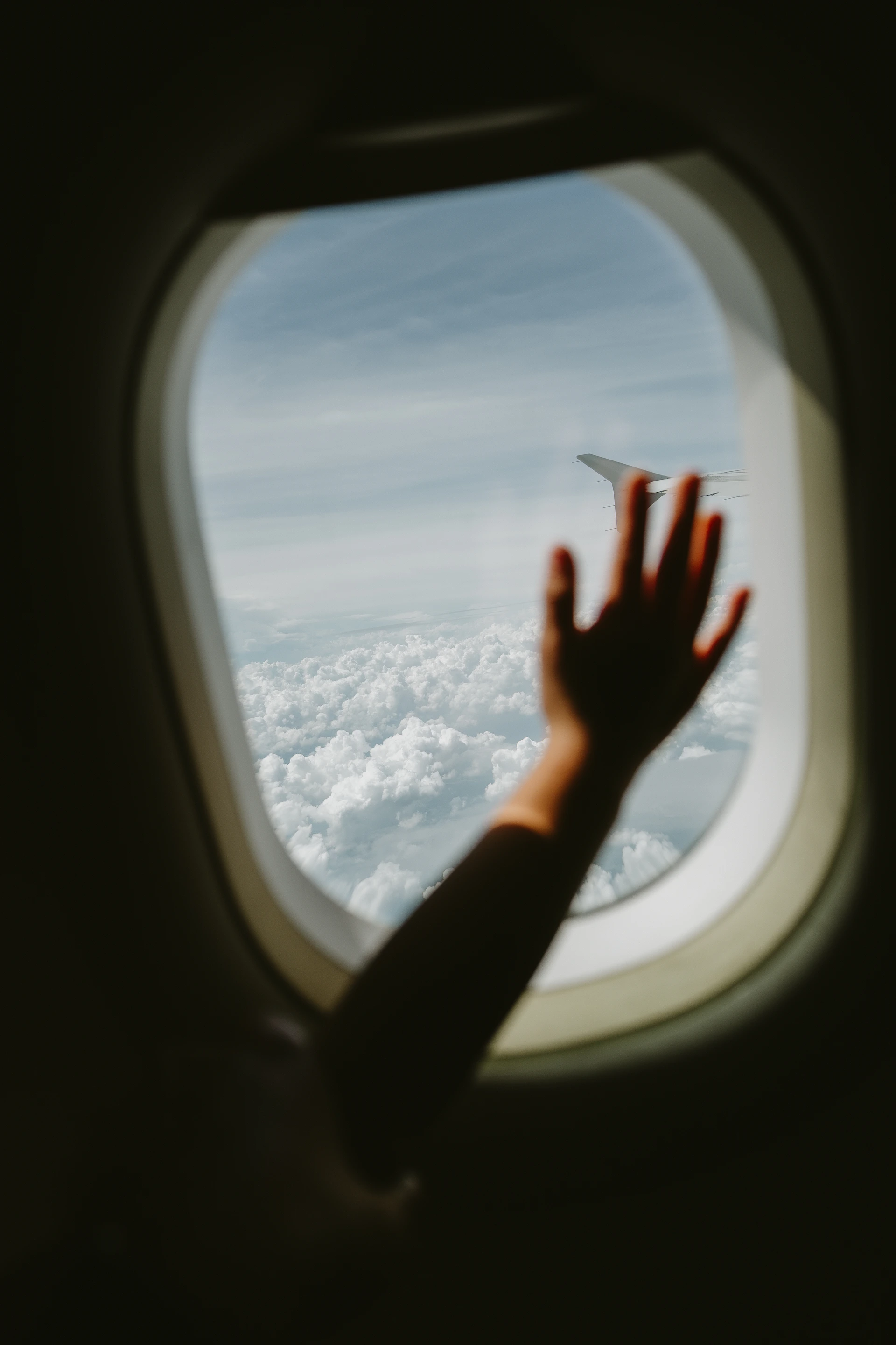 Hand reaching out airplane window to clouds