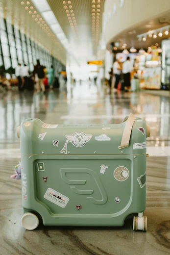 Green suitcase with travel stickers in airport terminal