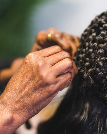 Hands braiding dark, curly hair with intricate detail.