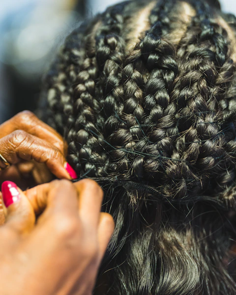 Hands braiding dark hair with red nails