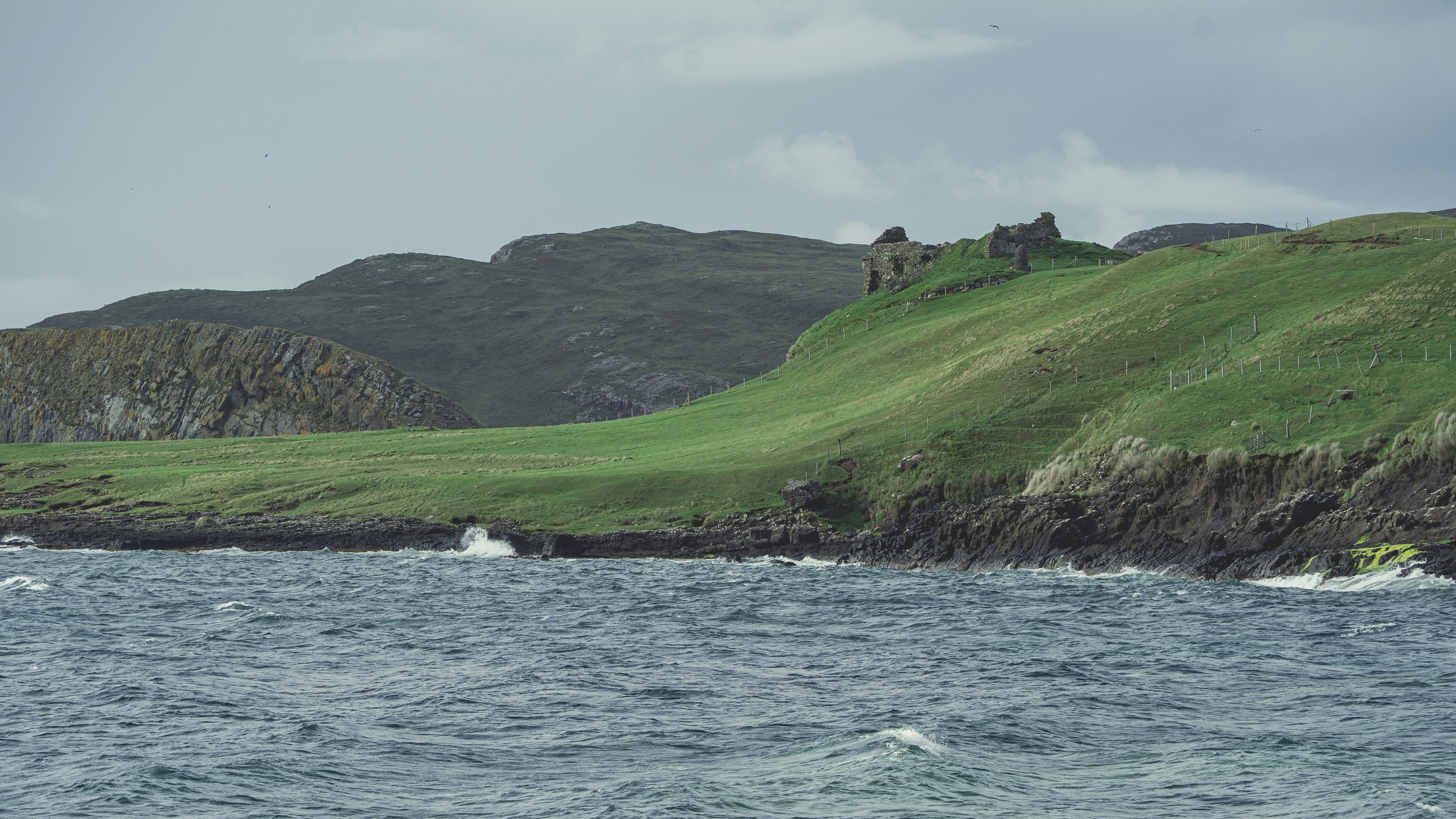 Ruined castle on a grassy hill overlooking the sea.