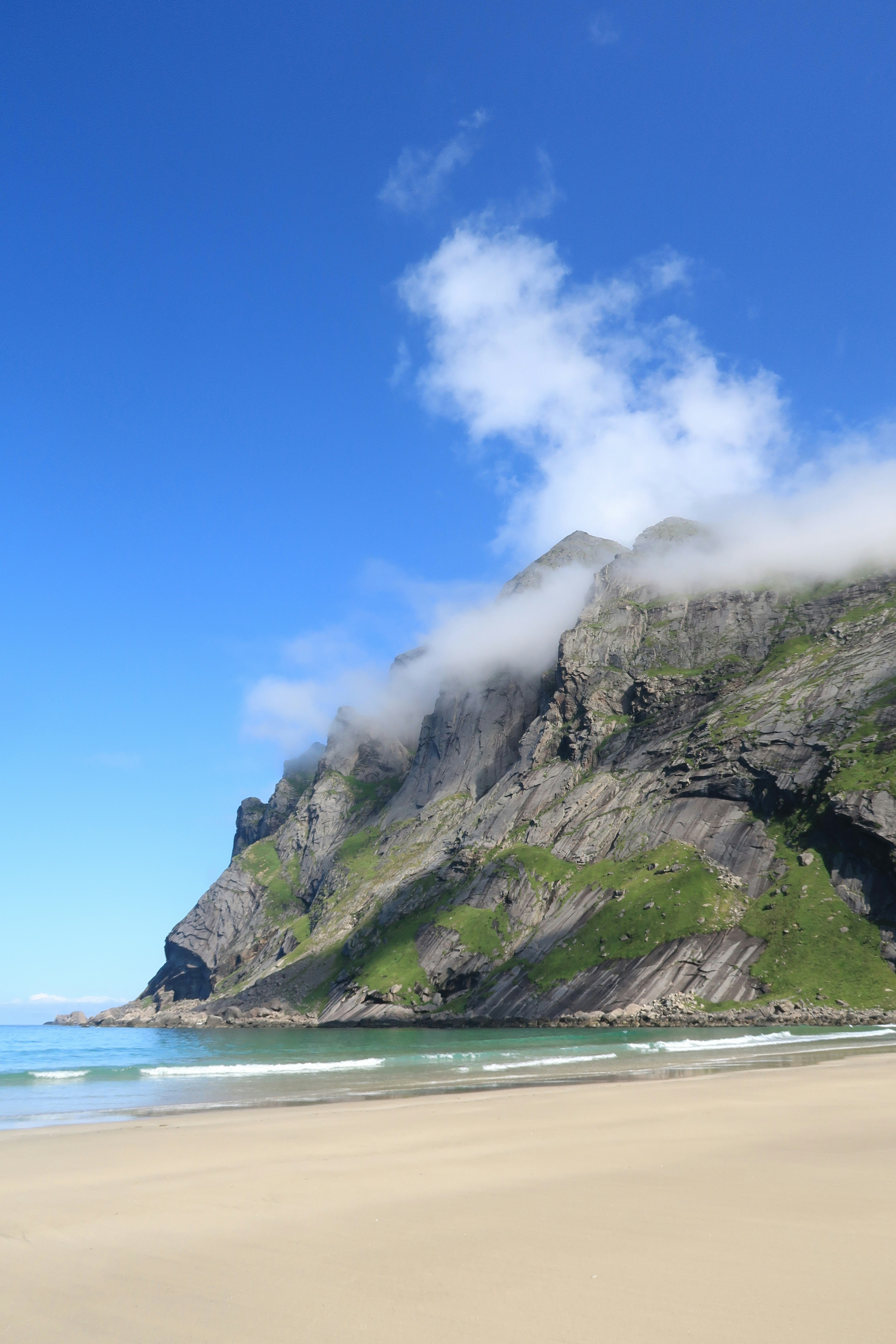 Sandy beach with a dramatic mountain shrouded in clouds.