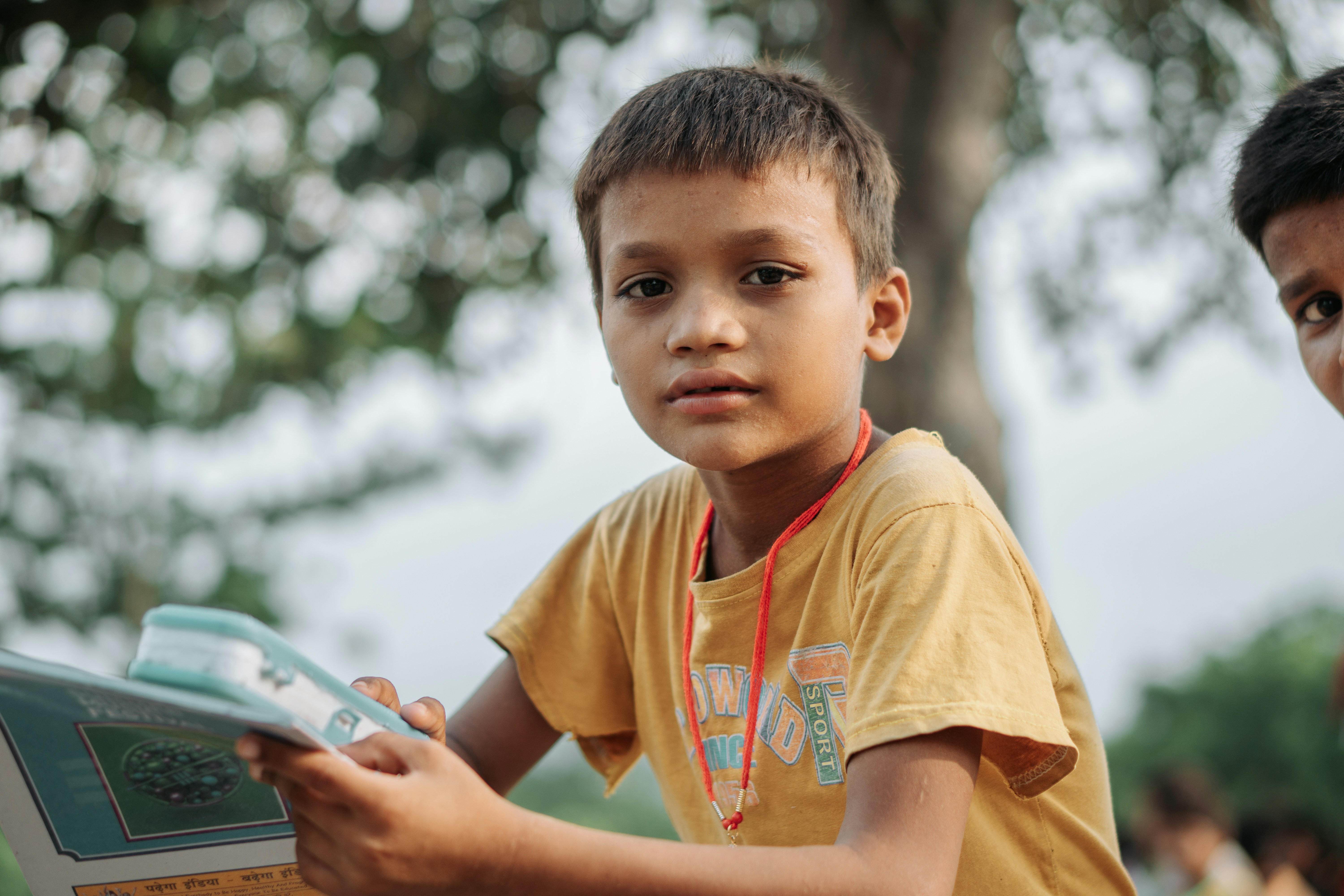 Young boy in yellow shirt reads a book outdoors.