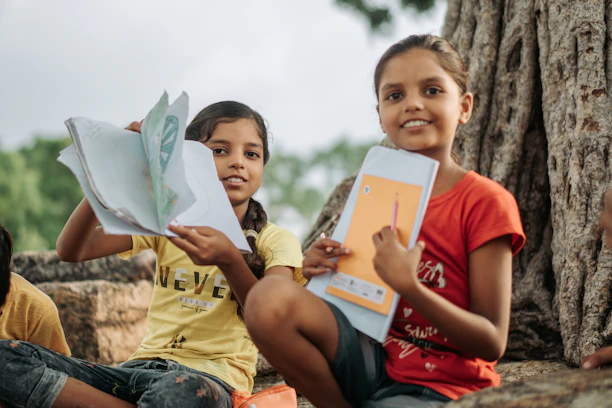 Two young girls holding books and folders outdoors.