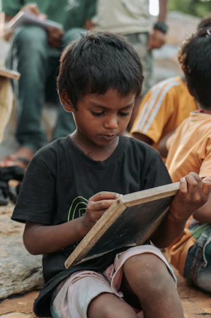 Young boy writing on a small chalkboard outdoors.
