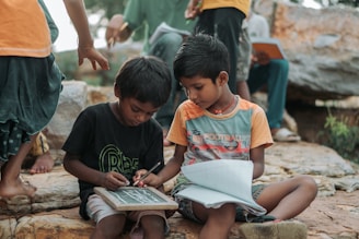 Two young boys learning outdoors with slate and notebook.