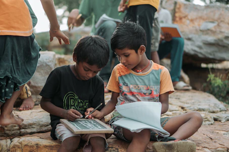 Two young boys learning outdoors with slate and notebook.