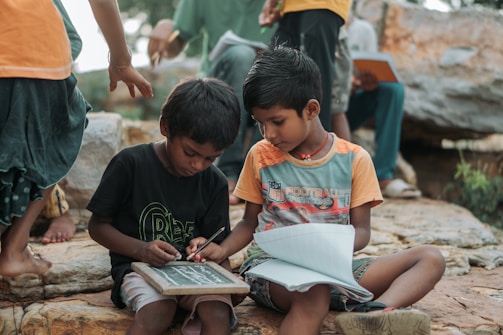 Two young boys learning outdoors with slate and notebook.