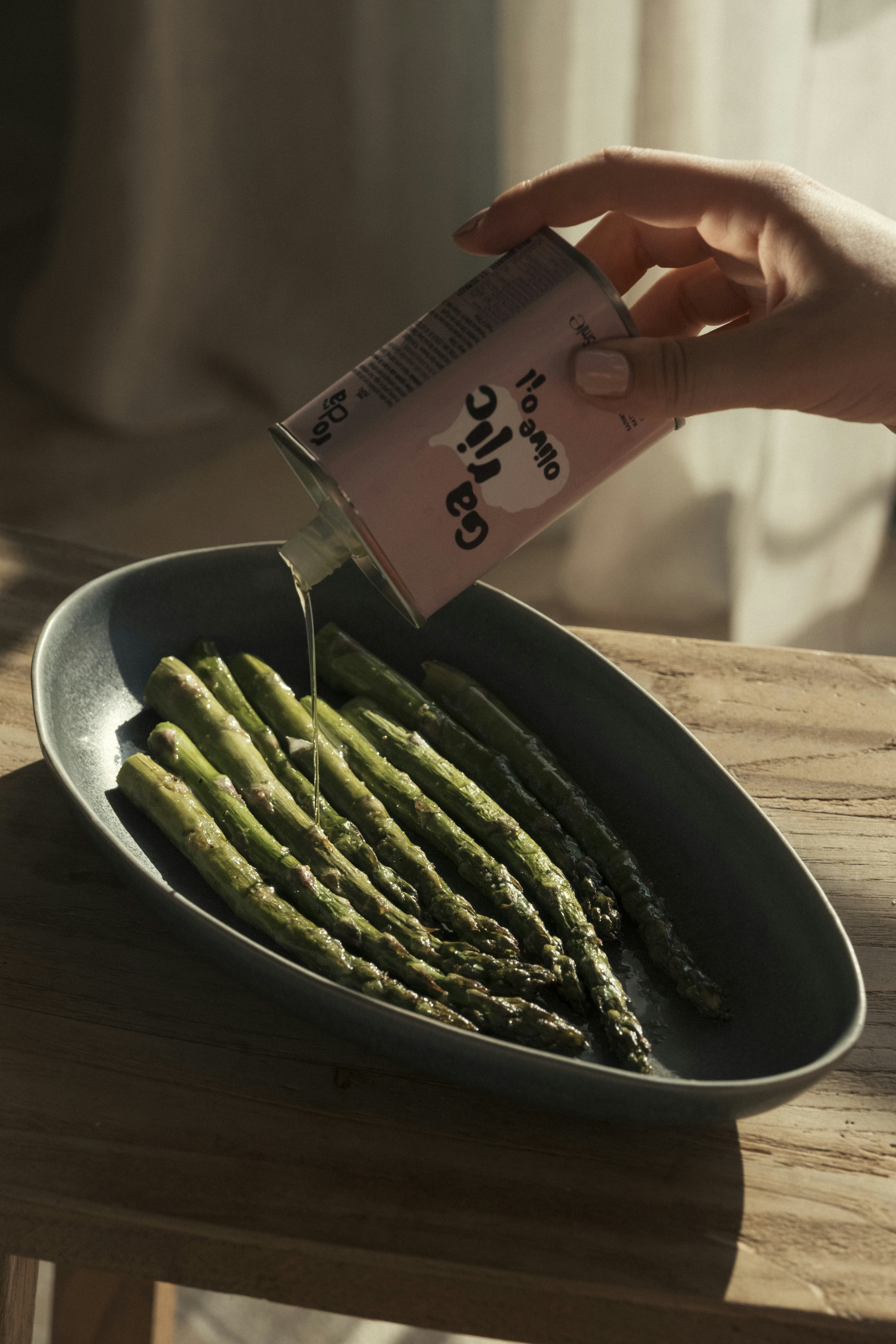 Hand pouring olive oil onto roasted asparagus in a bowl