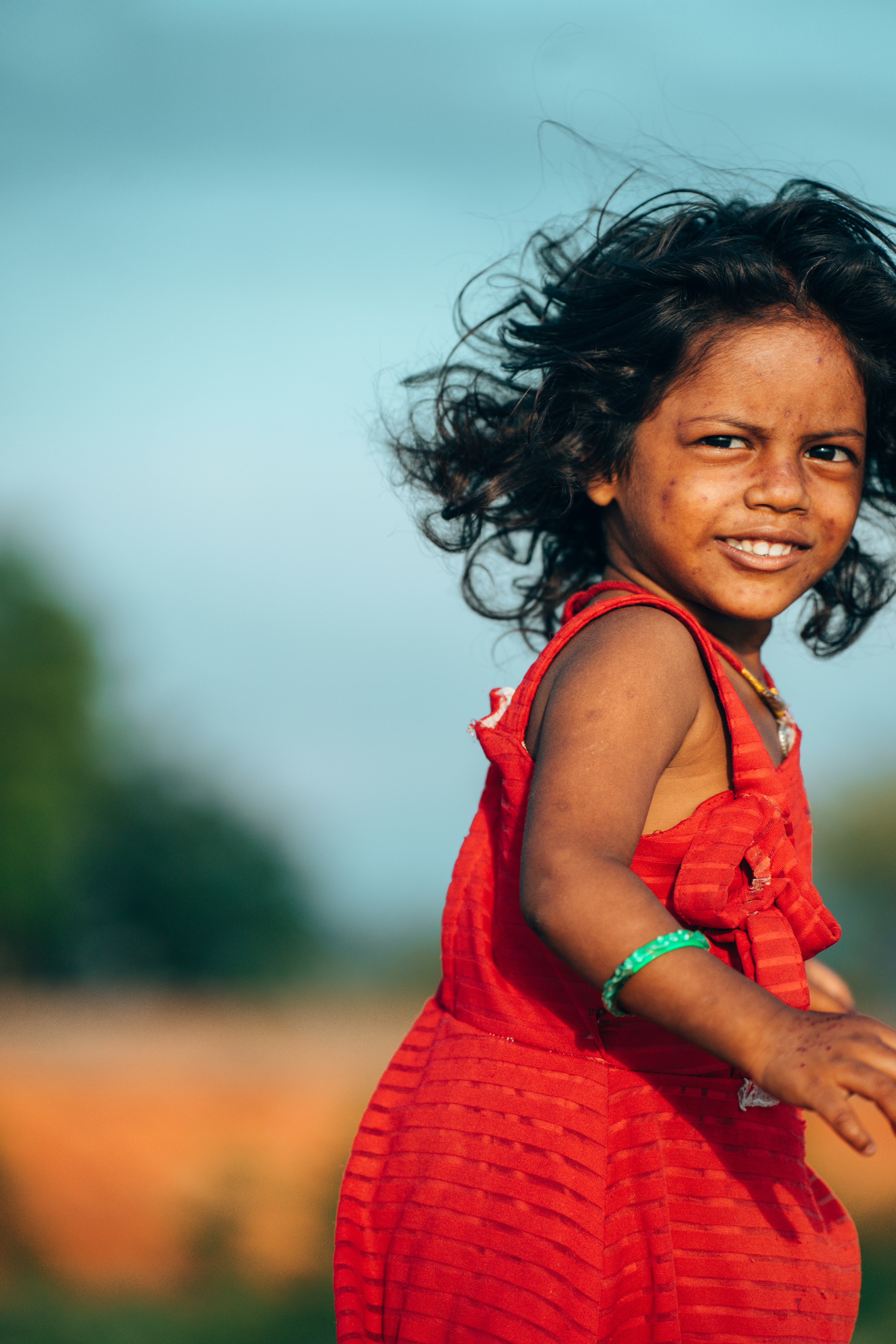 A young girl in a red dress smiles outdoors