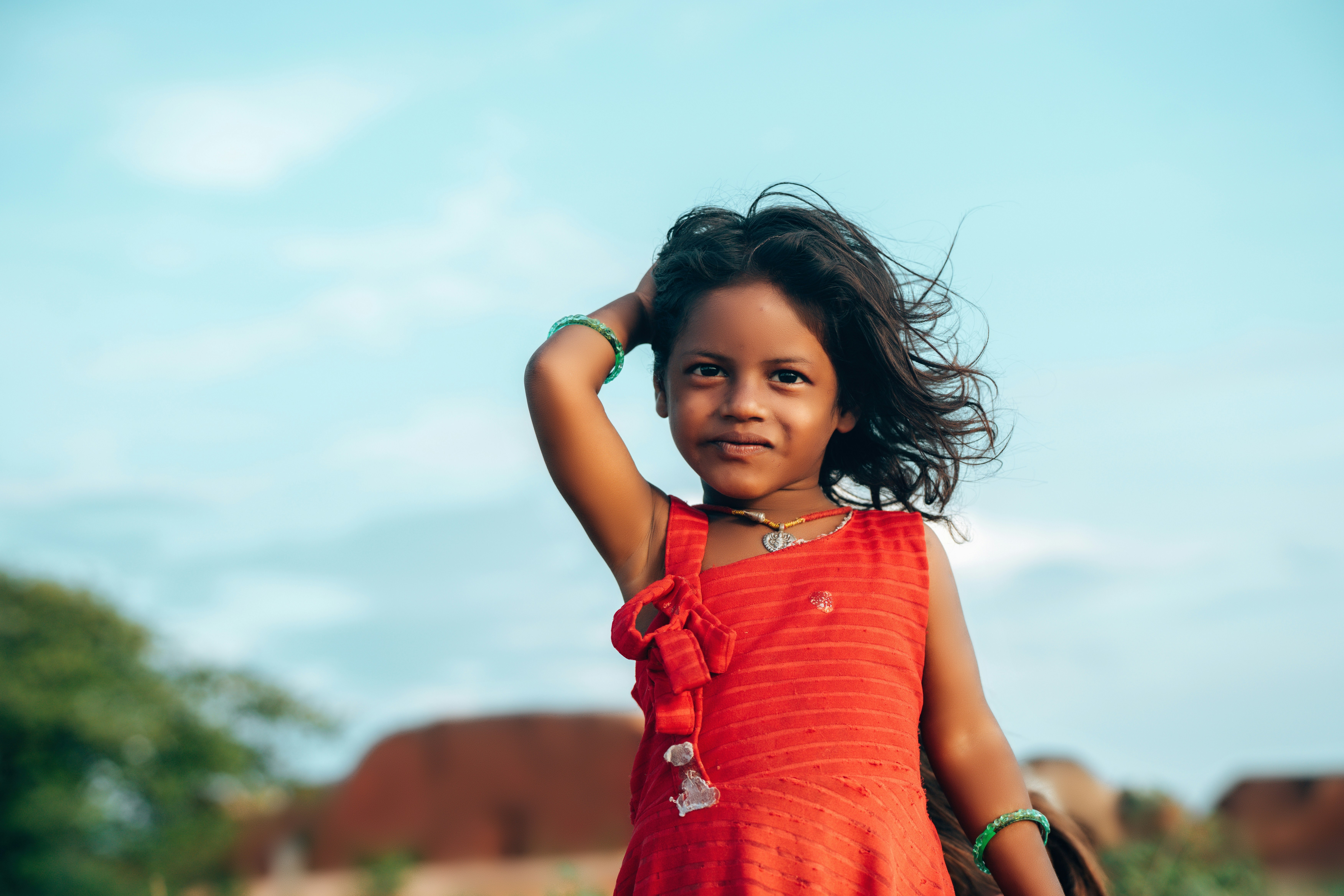 A young girl in a red dress smiles outdoors.