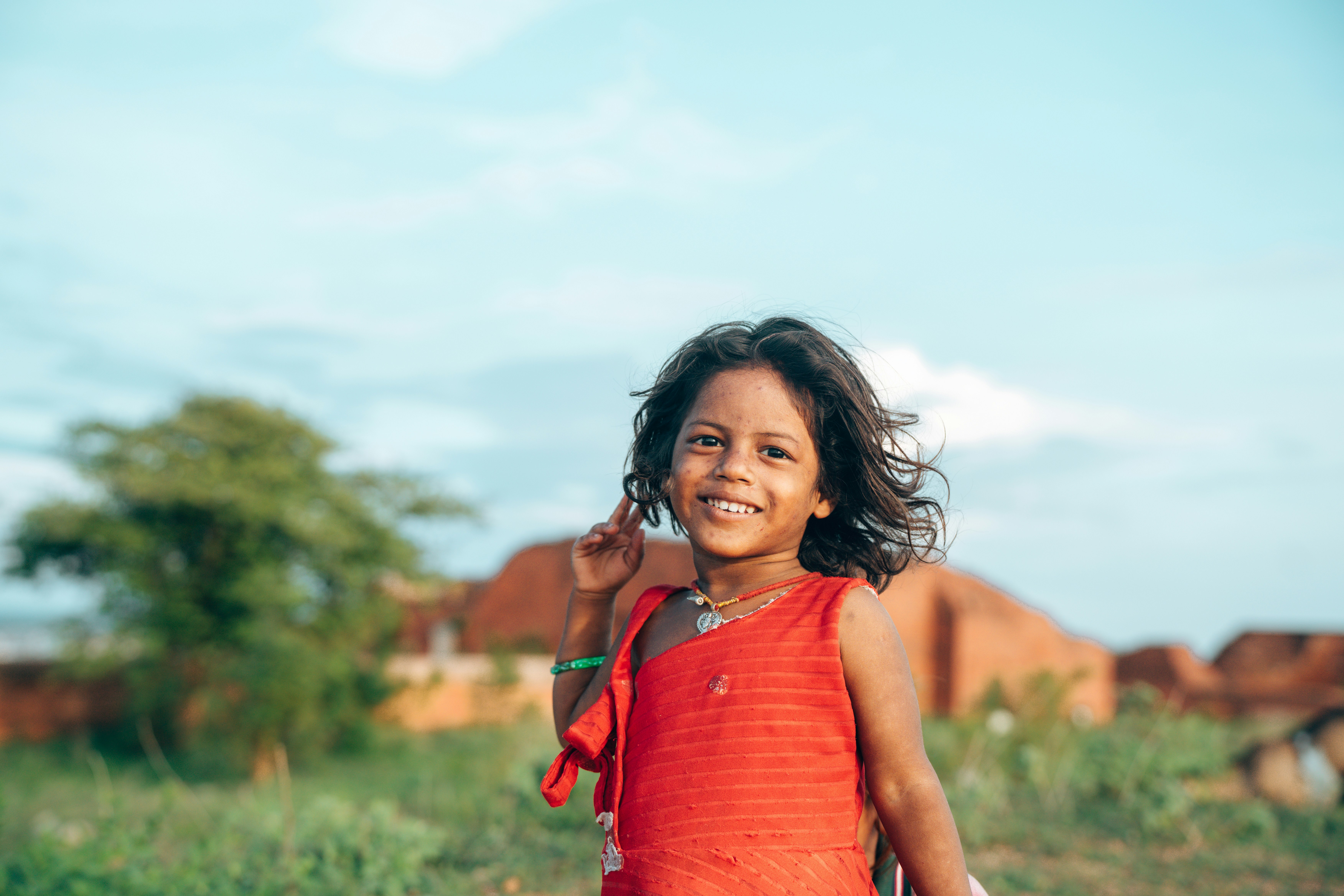 A young girl smiles and holds up peace sign.