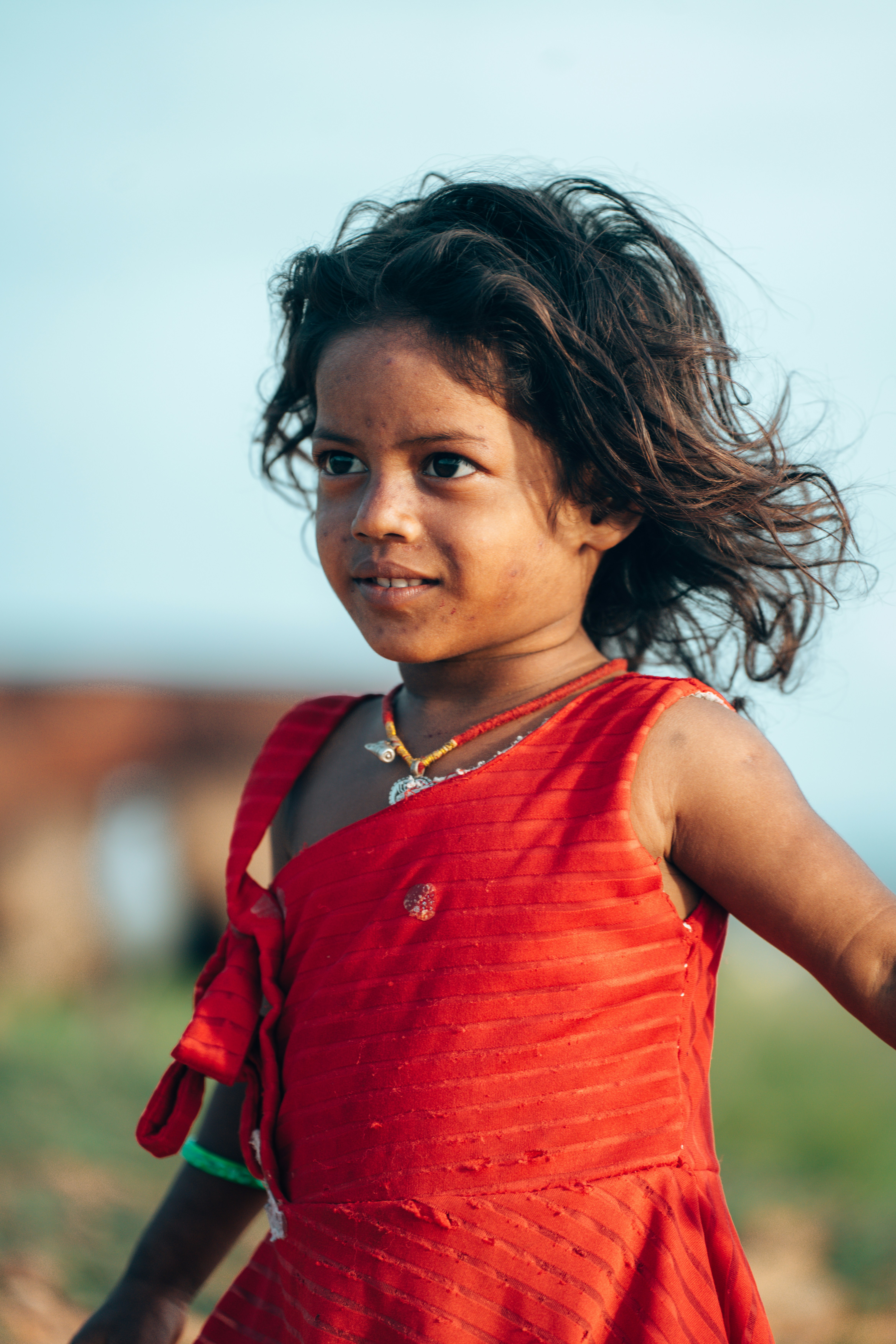A young girl in a red dress smiles outdoors.