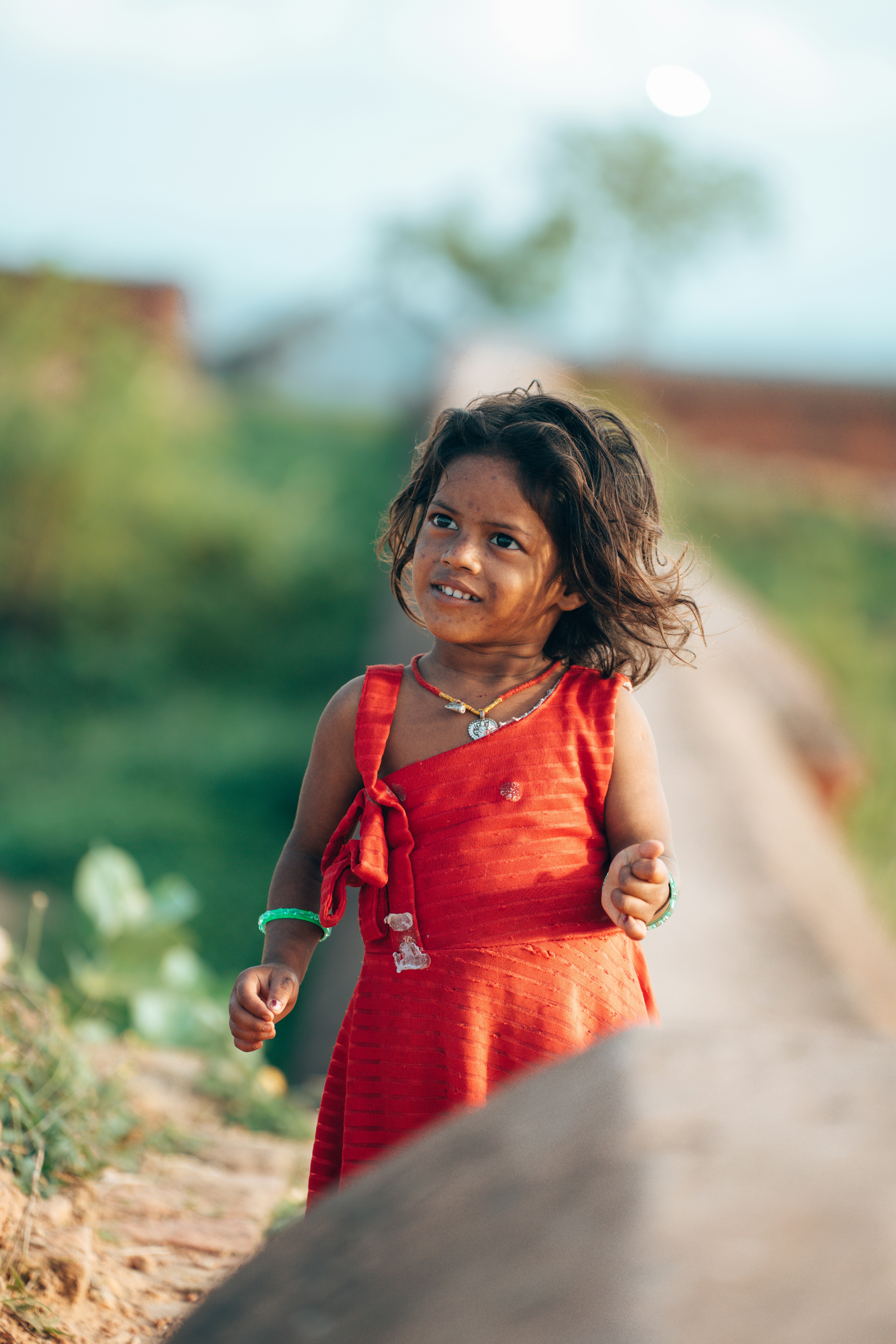 A young girl in a red dress smiles outdoors.