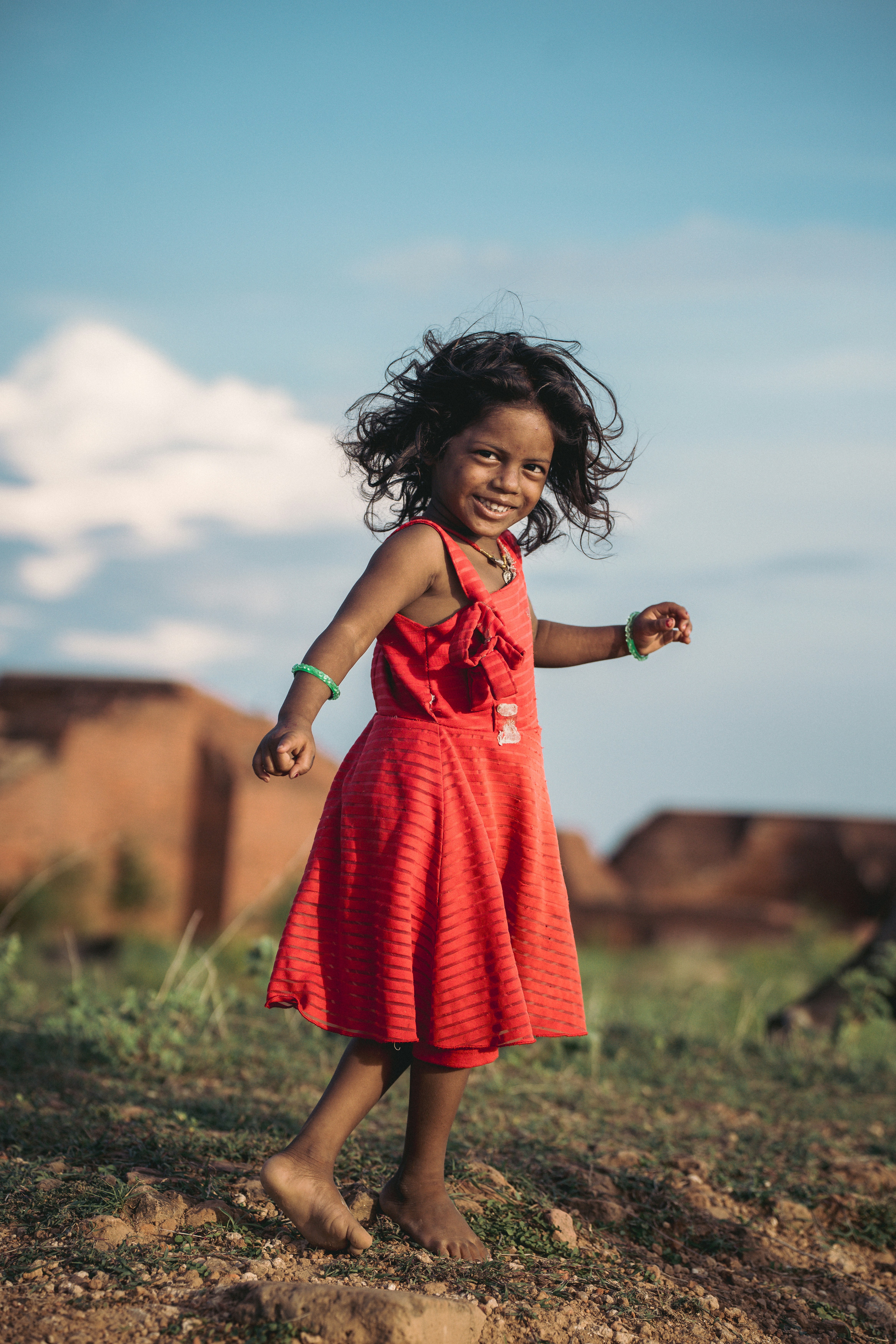 A young girl in a red dress smiles outdoors.