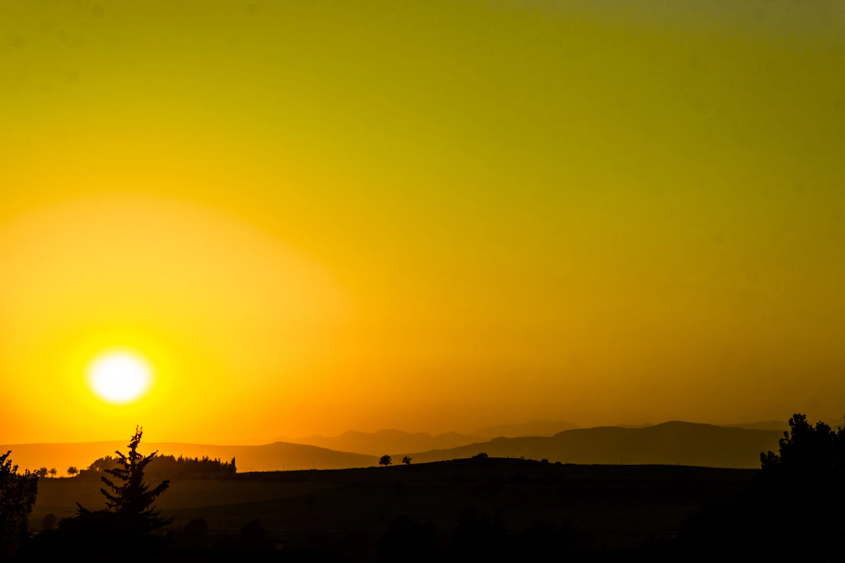 Golden sun setting over silhouetted hills at dusk.
