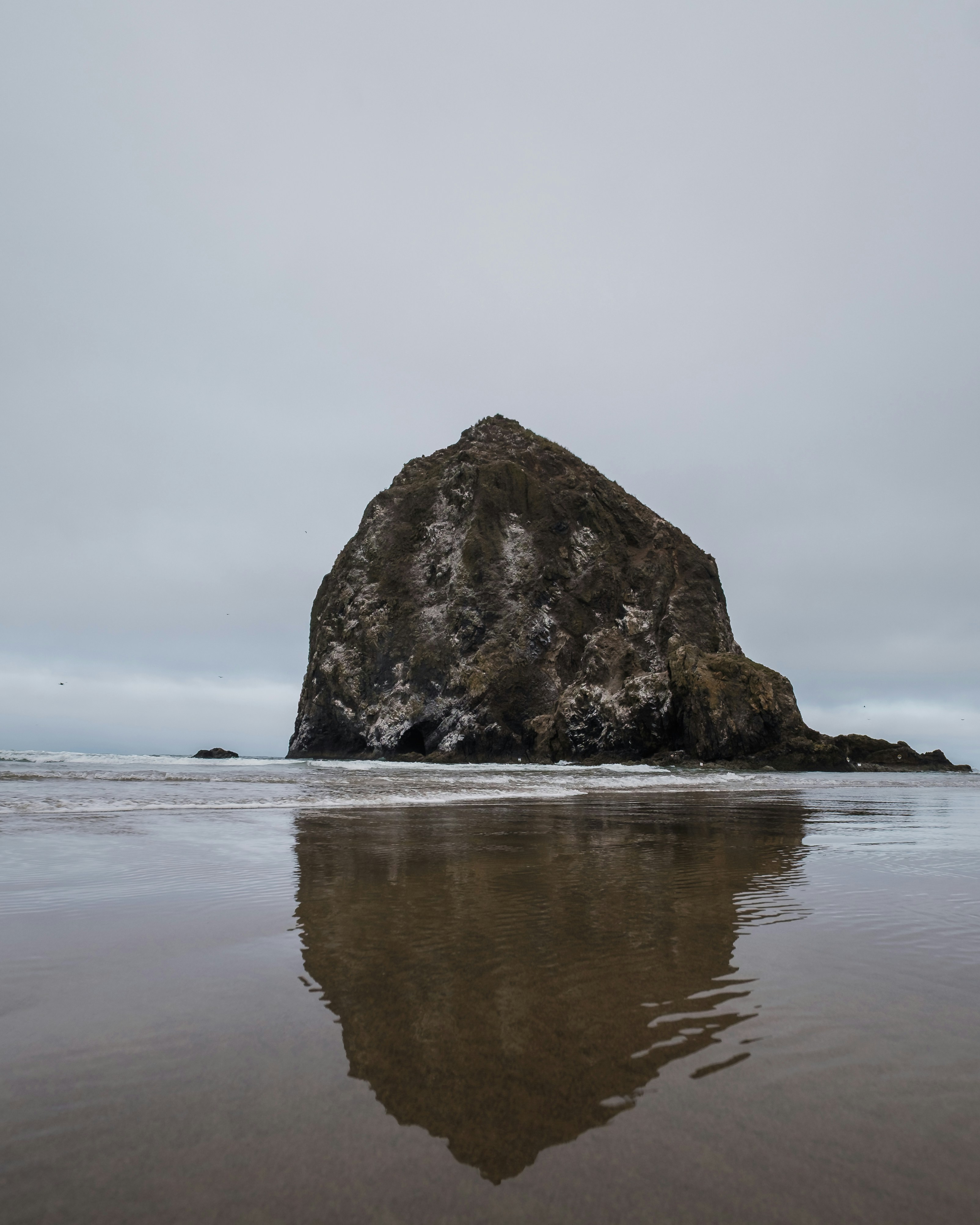 Gran formación rocosa reflejada en arena húmeda durante la marea baja