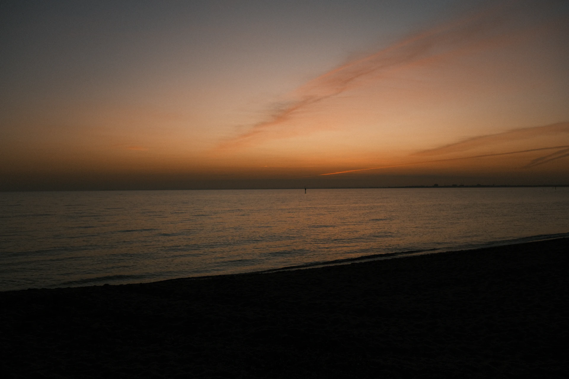Calm ocean at dusk with a faint cloud streak.