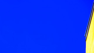 Bright yellow building corner against vivid blue sky.