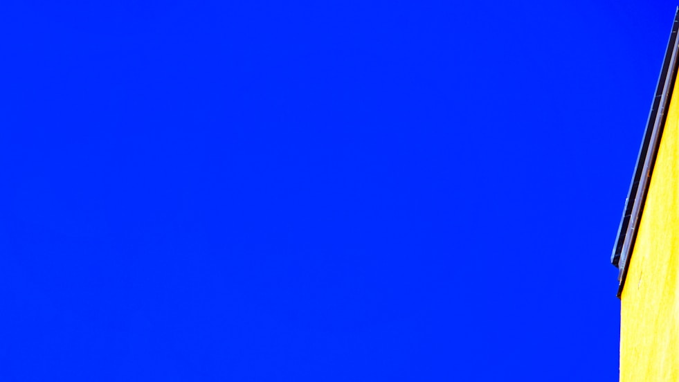 Bright yellow building corner against vivid blue sky.