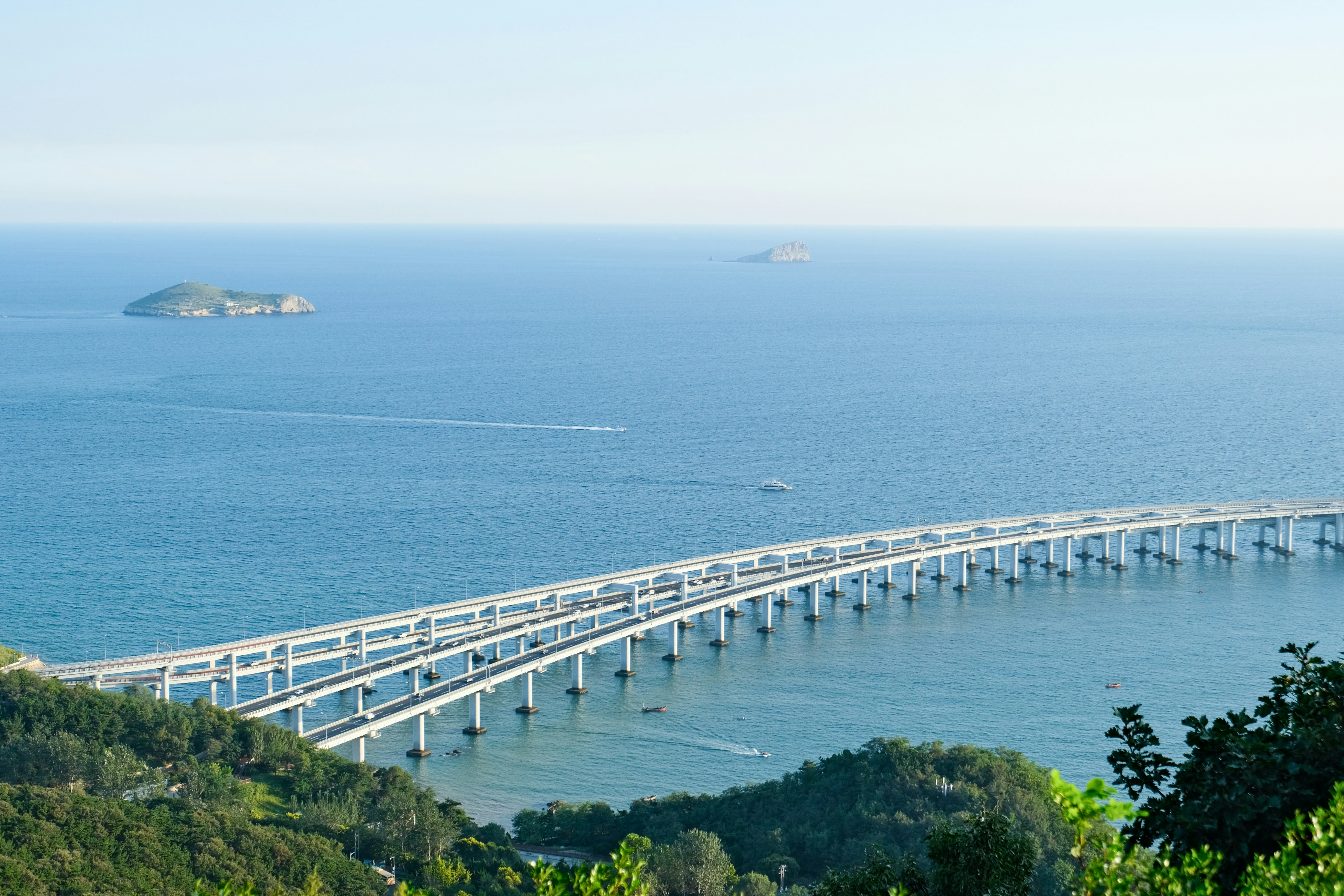 Long bridge over blue ocean with distant island.