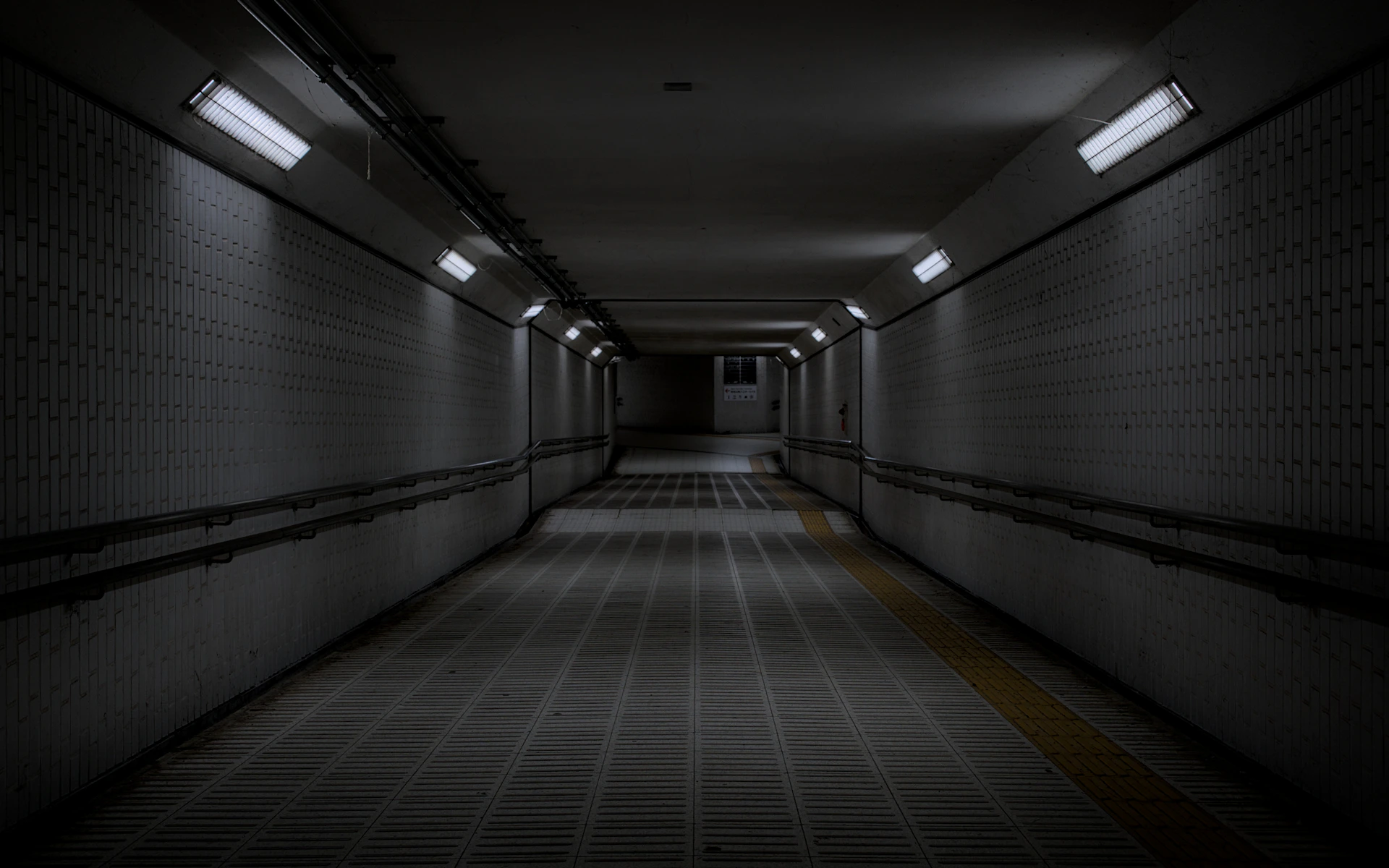 Dimly lit underground pedestrian tunnel with tiled walls.