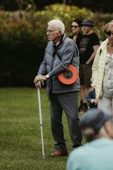 Elderly man with cane standing in a park.