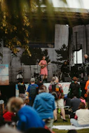 Musician performs on outdoor stage for seated audience.