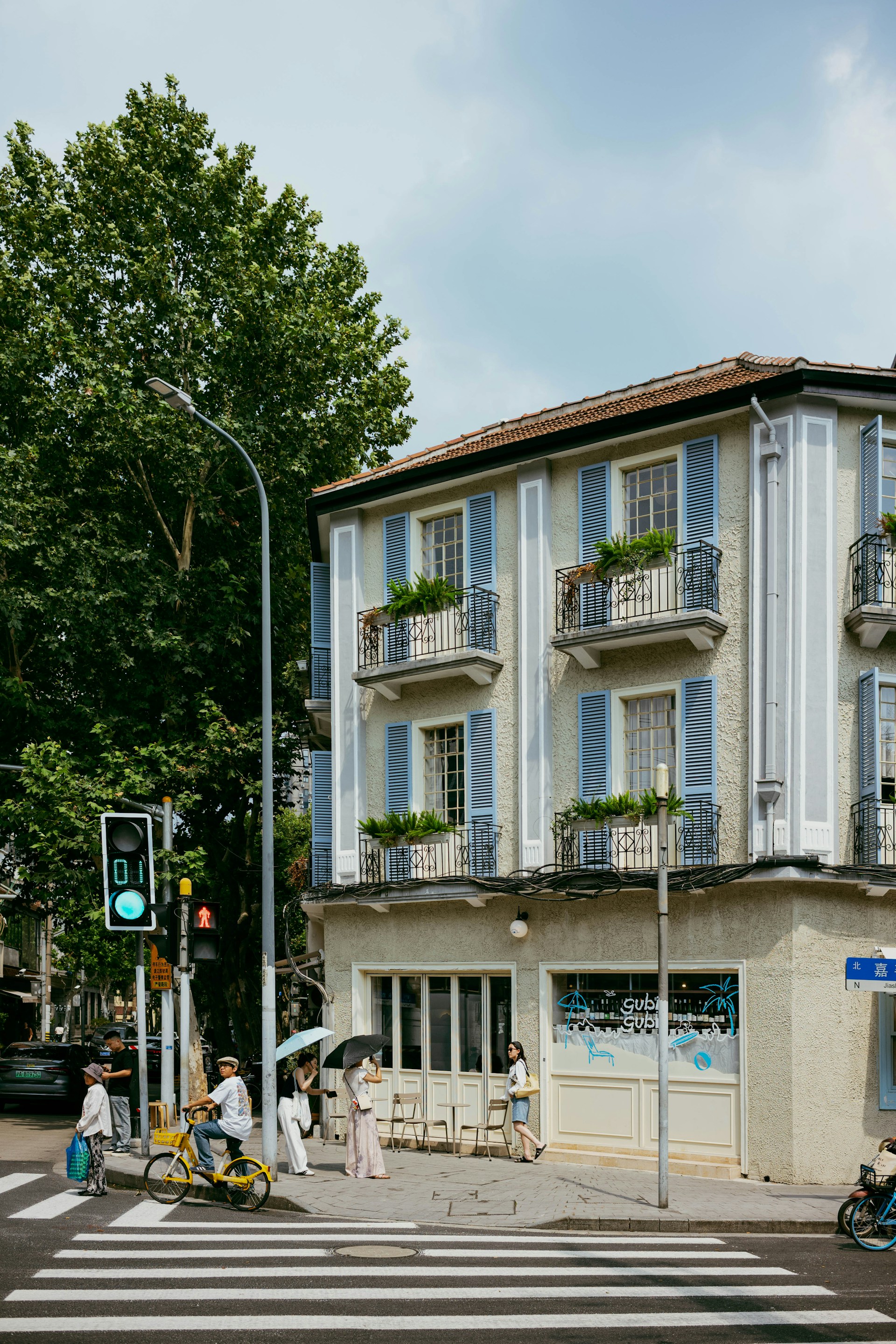 People crossing street near building with blue shutters.