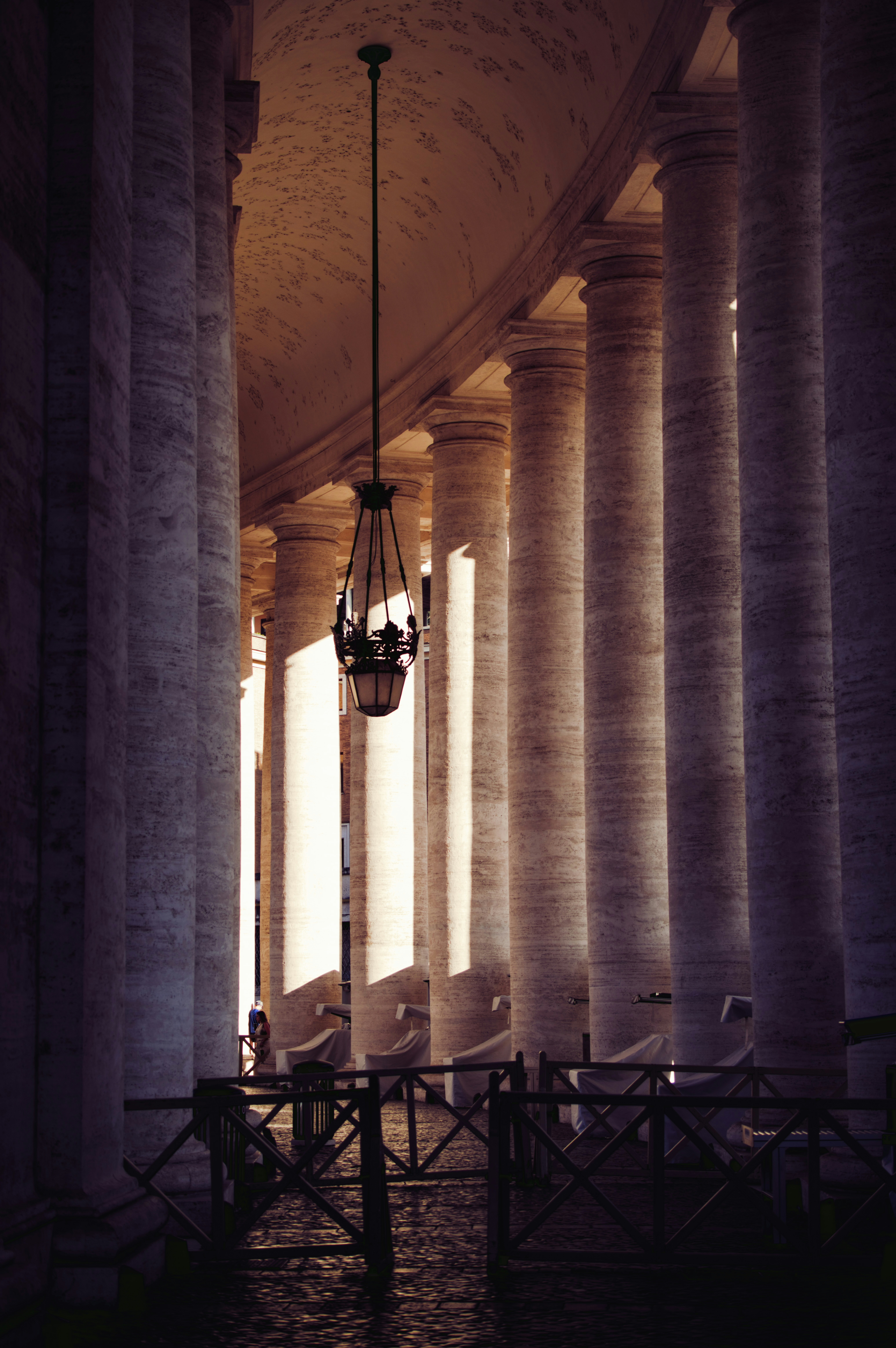 Grand colonnade with a hanging lamp and sunlight.