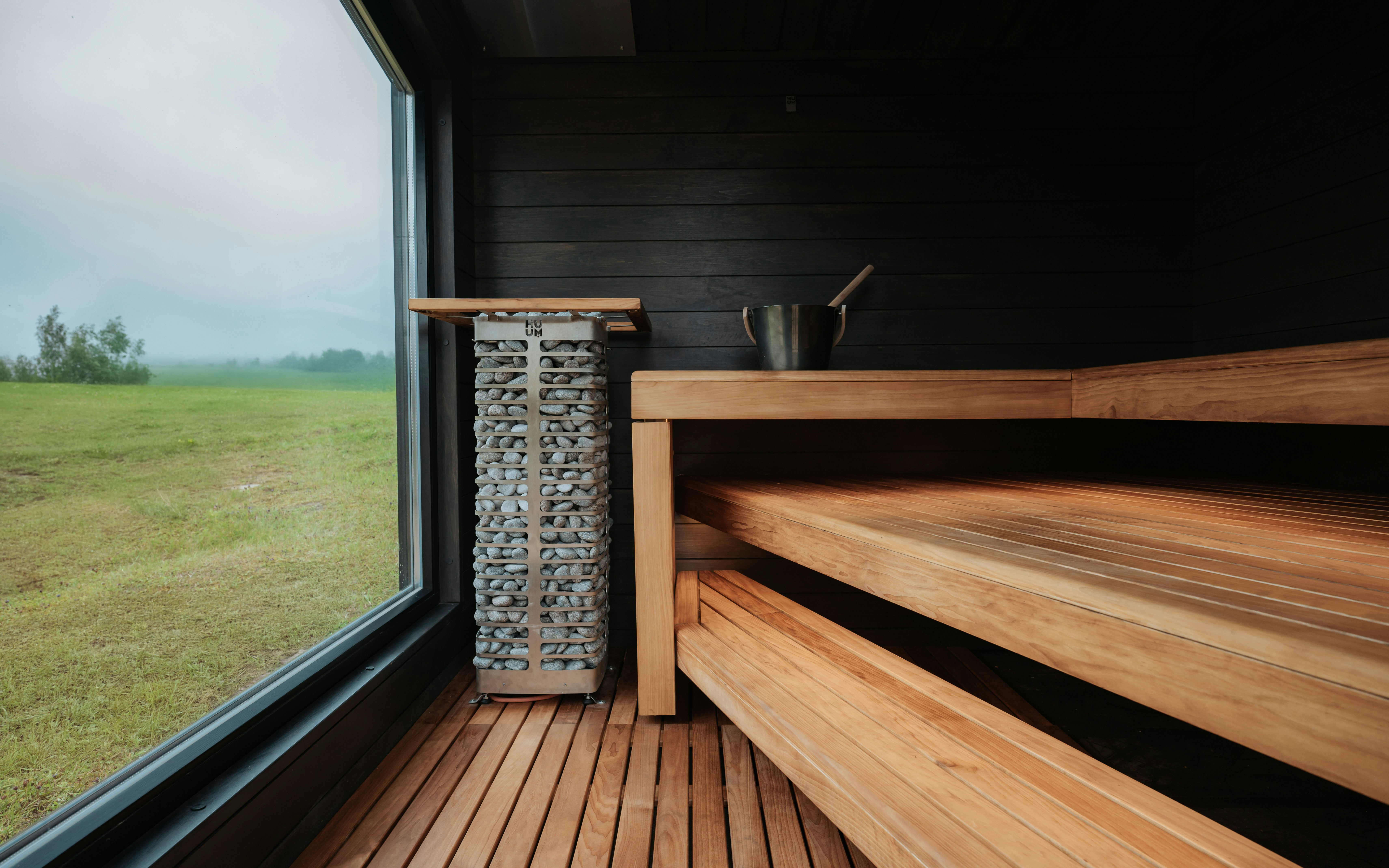 A stylish sauna interior featuring wooden benches, a tall stone heater, and contrasting dark wall panels. The design blends natural warmth with modern spa aesthetics for a calming wellness experience.