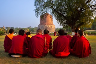 Monks in red robes sit in a circle outdoors.