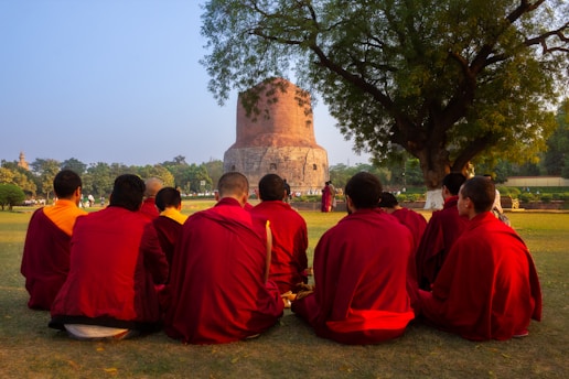 Monks in red robes sit in a circle outdoors.