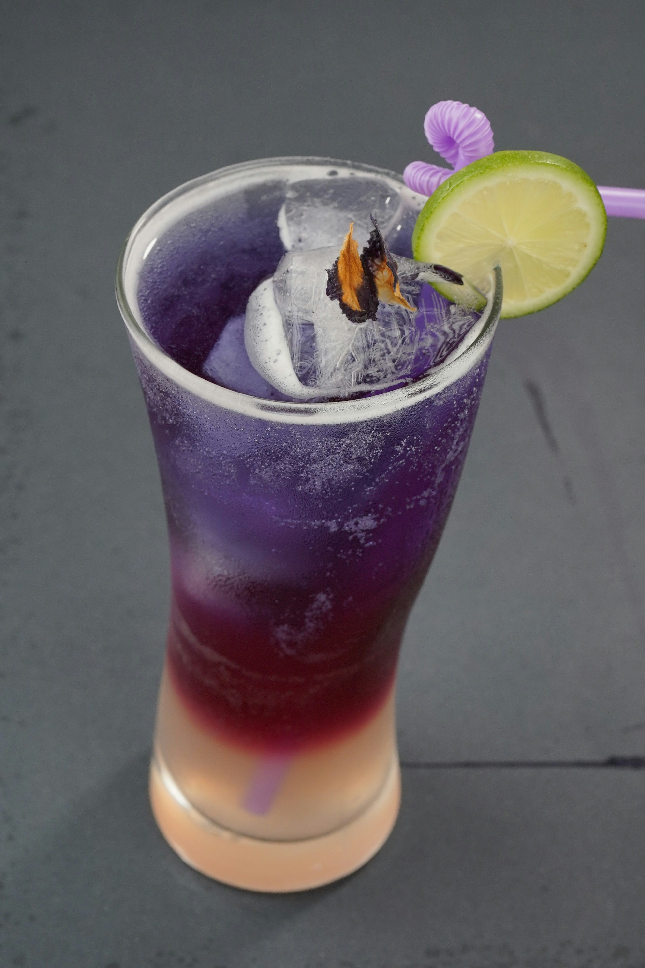 Una bebida morada y rosa en capas con hielo y lima.