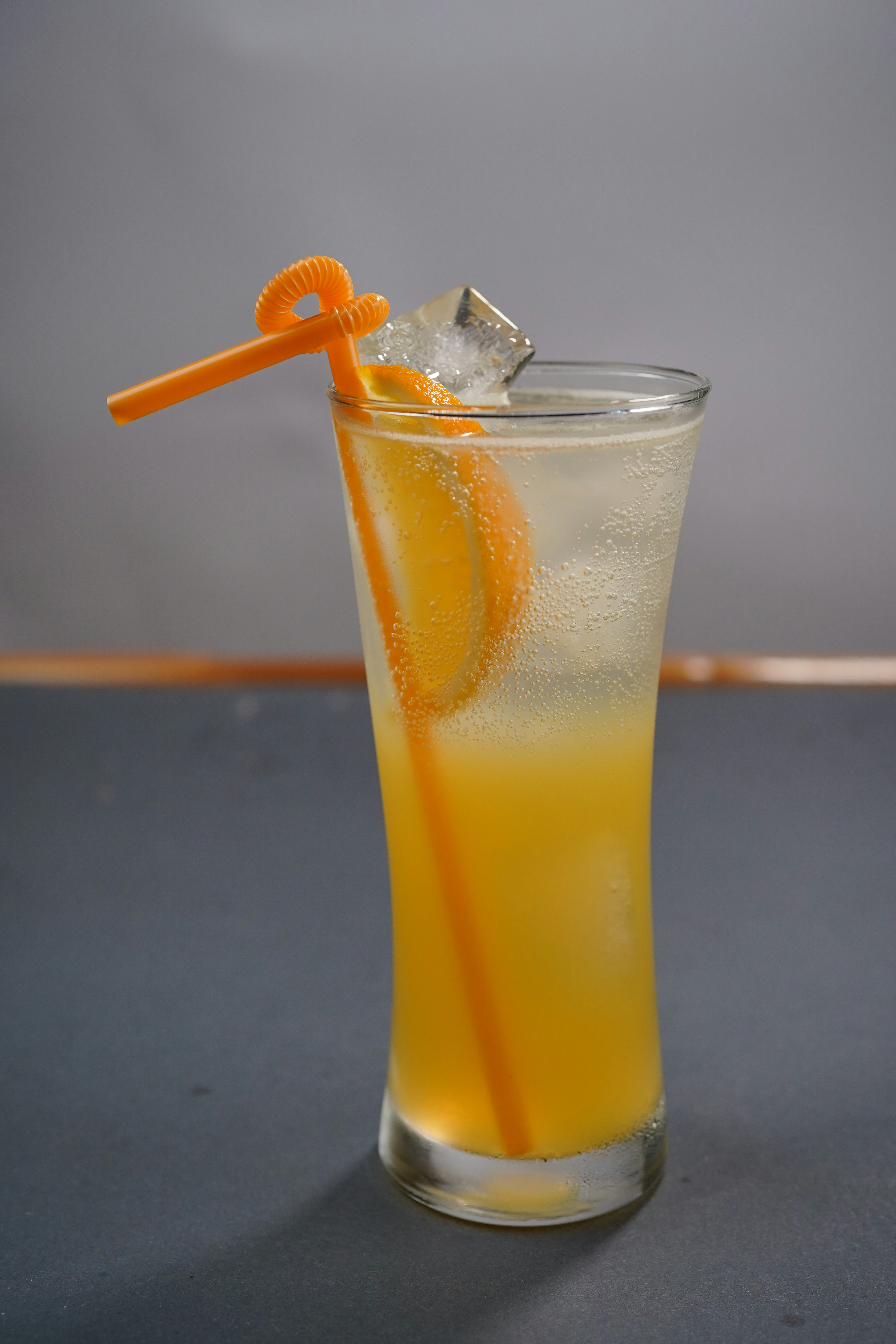 Vaso alto de jugo de naranja con hielo y pajita.