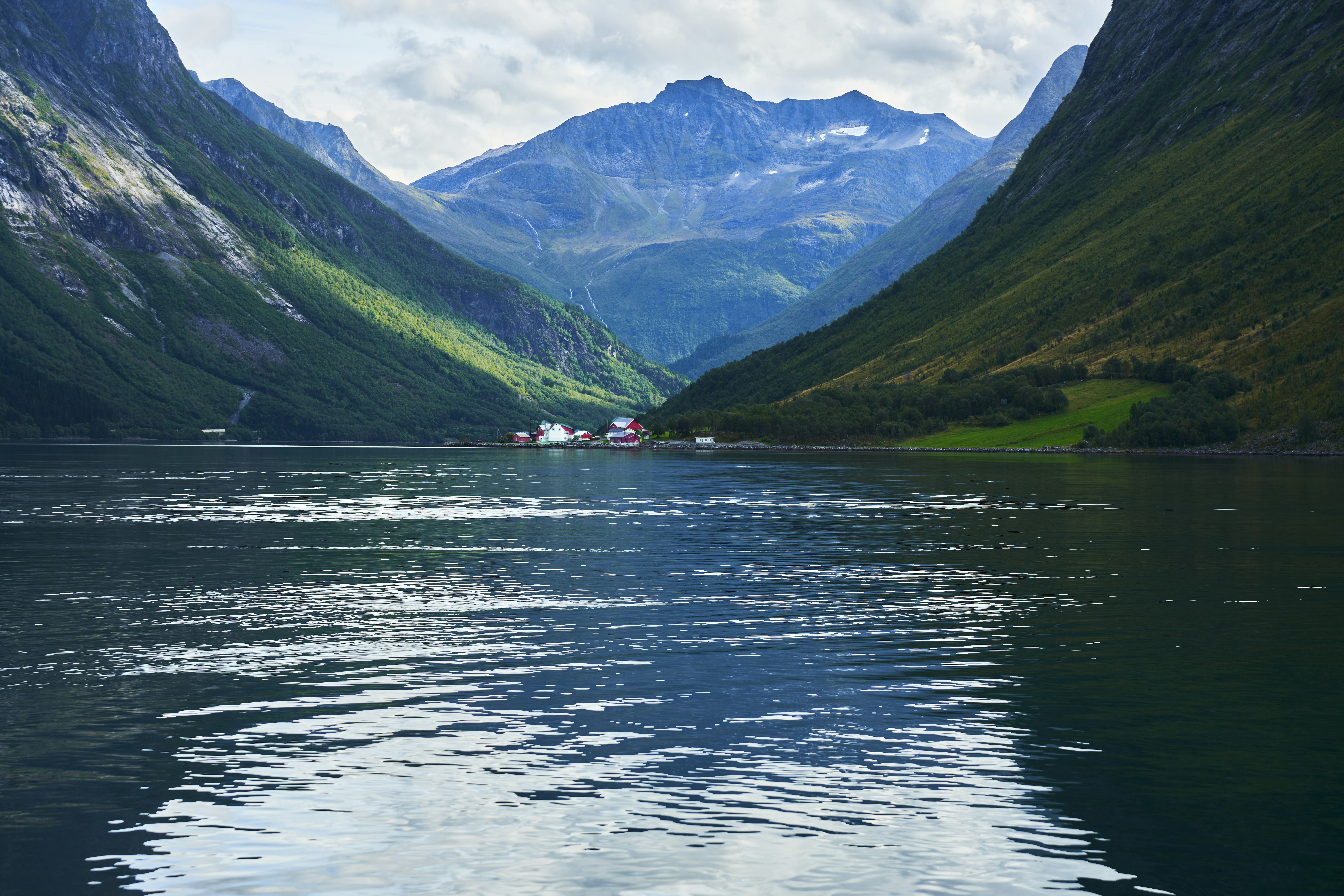 Ruhiger See reflektiert grüne Berge unter bewölktem Himmel