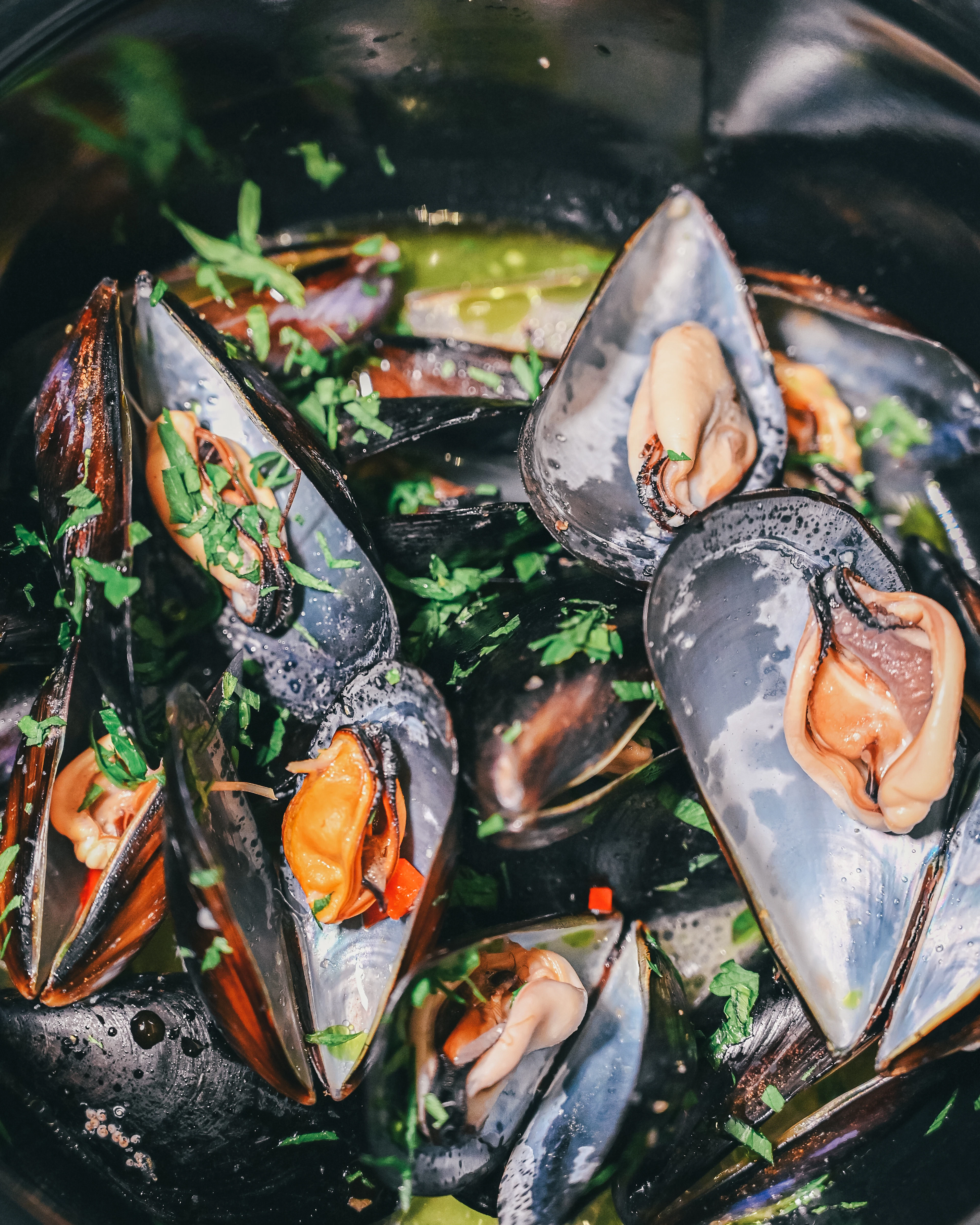 A dark pot of steamed mussels opened in a herb-flecked broth, scattered with chopped parsley and slivers of red chilli.