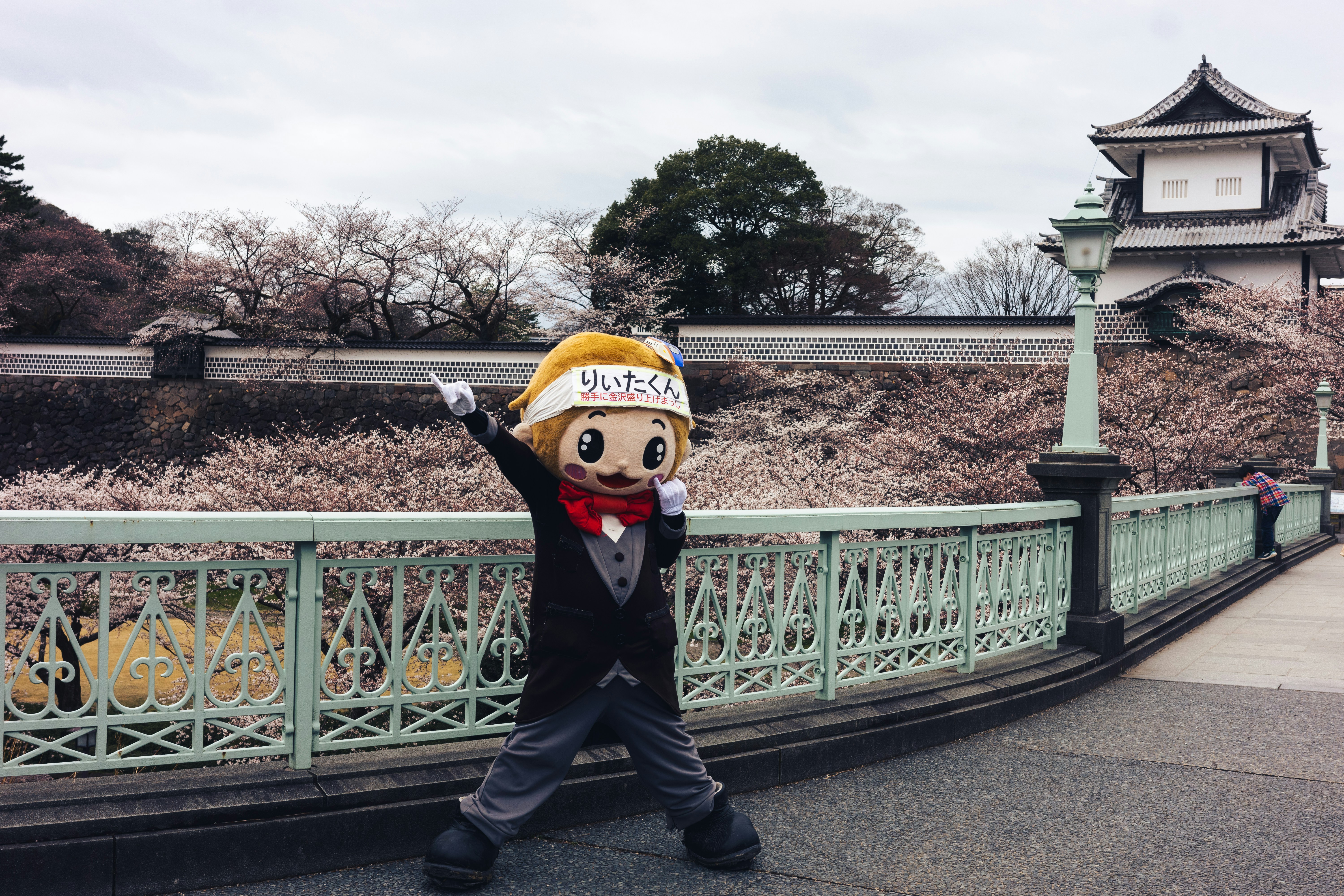 Mascot character poses by cherry blossoms and castle