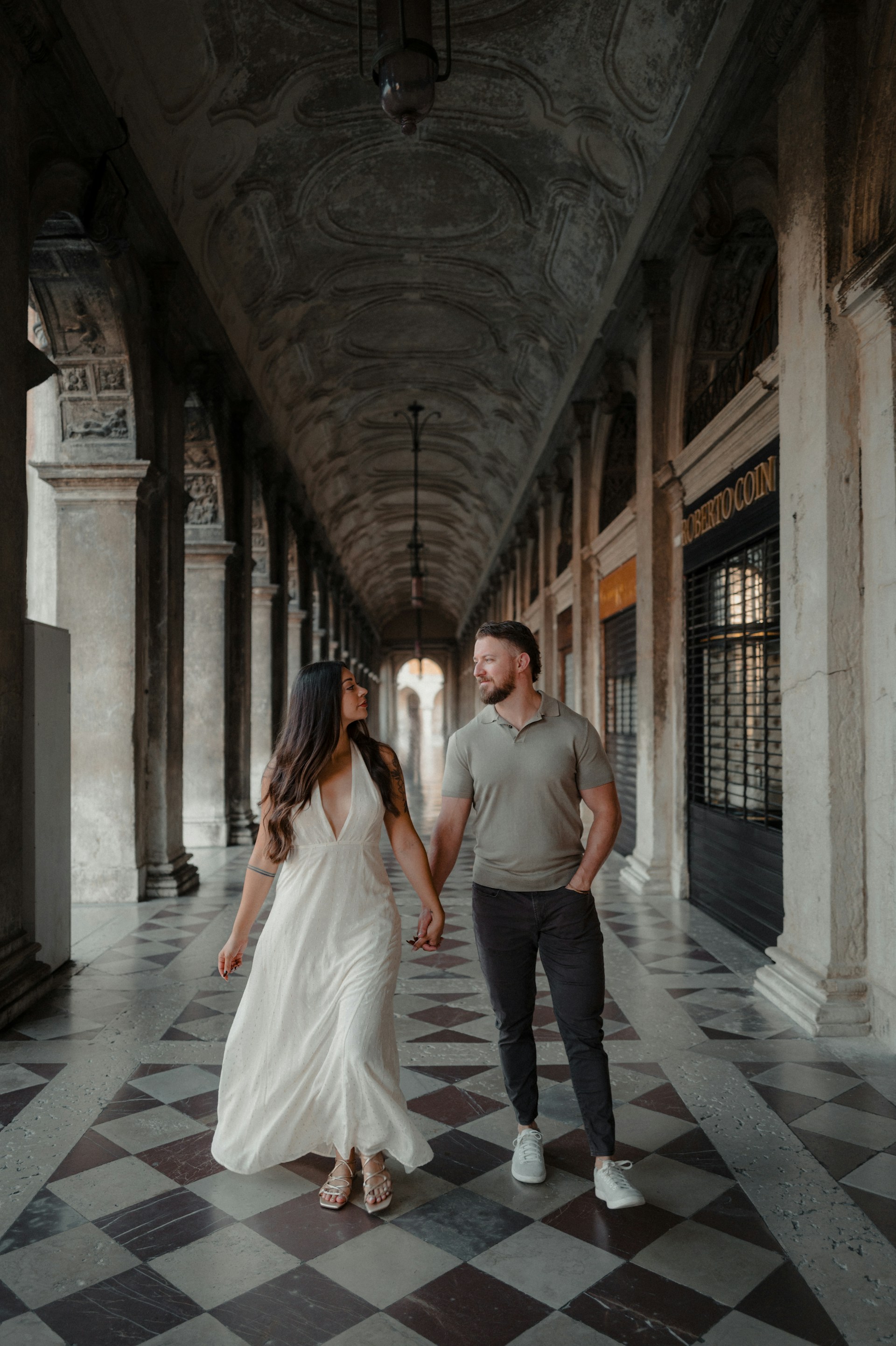 Couple holding hands walking through arched colonnade