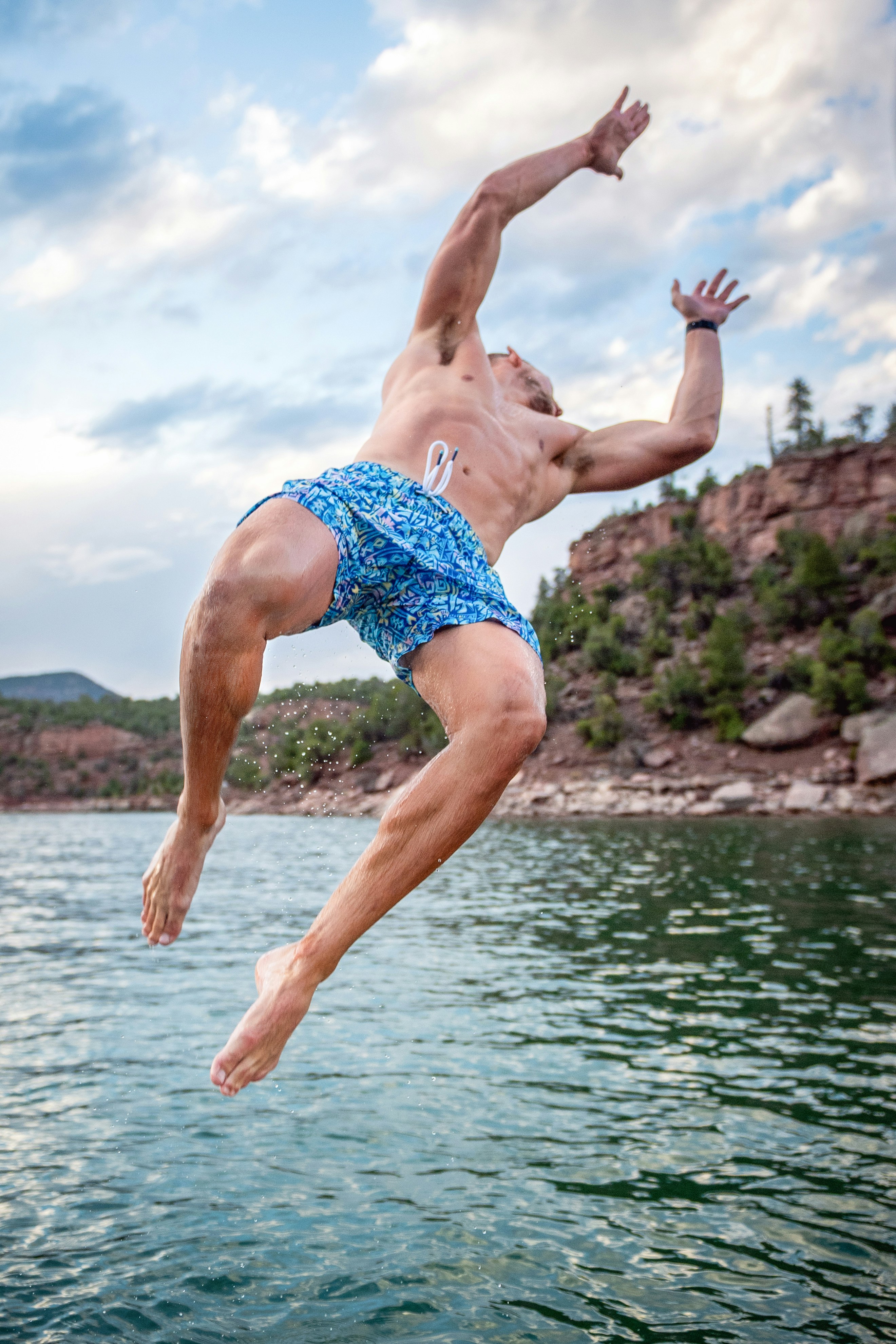 Man in patterned shorts jumps into a lake