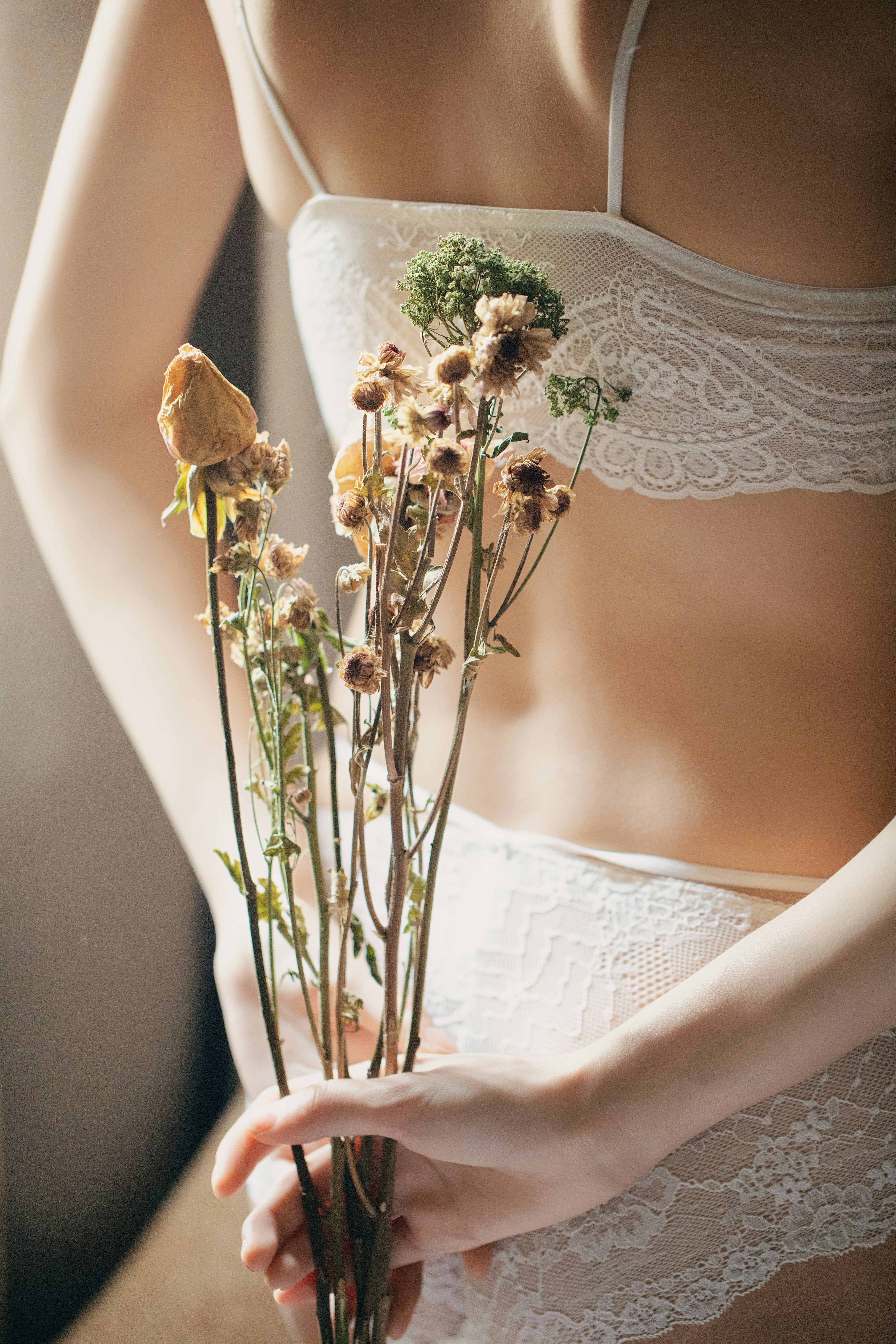 Woman in lingerie holding dried flowers behind back