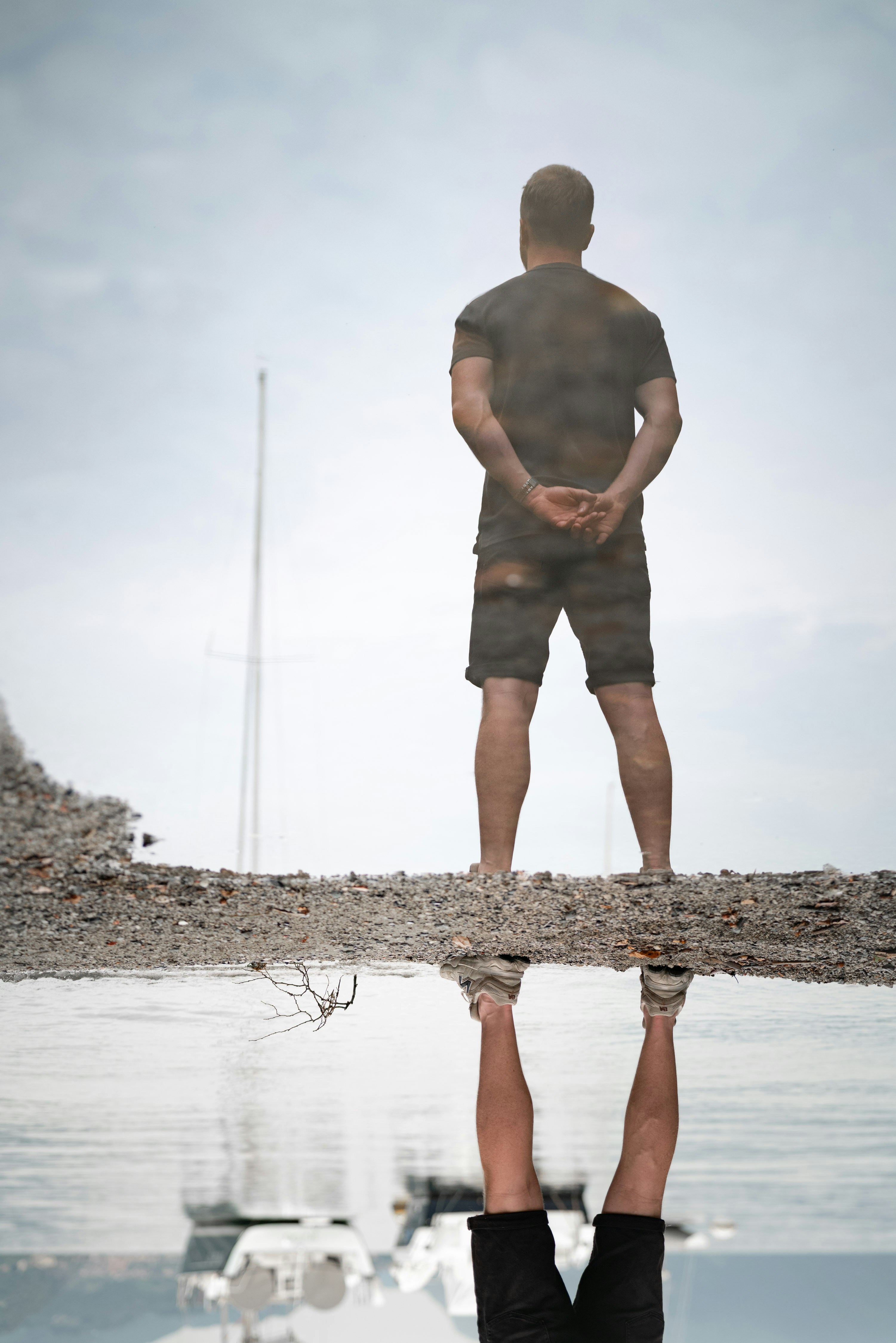 Homme debout près de l’eau avec reflet du bateau.