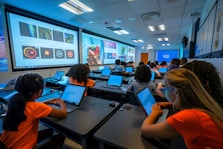 Students using laptops in a classroom with large screens.
