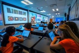 Students using laptops in a classroom with large screens.