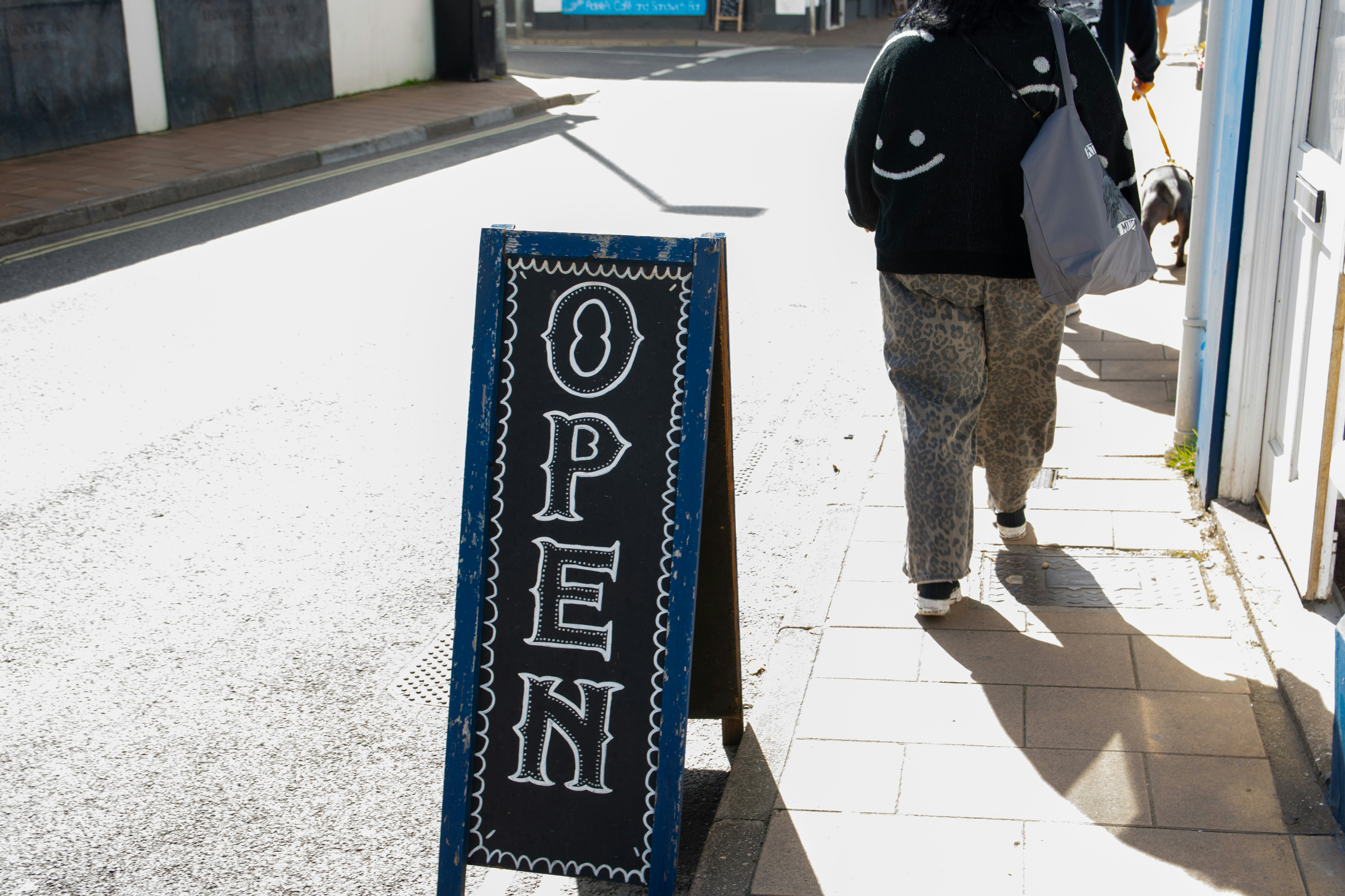 Open sign on sidewalk with person walking past.